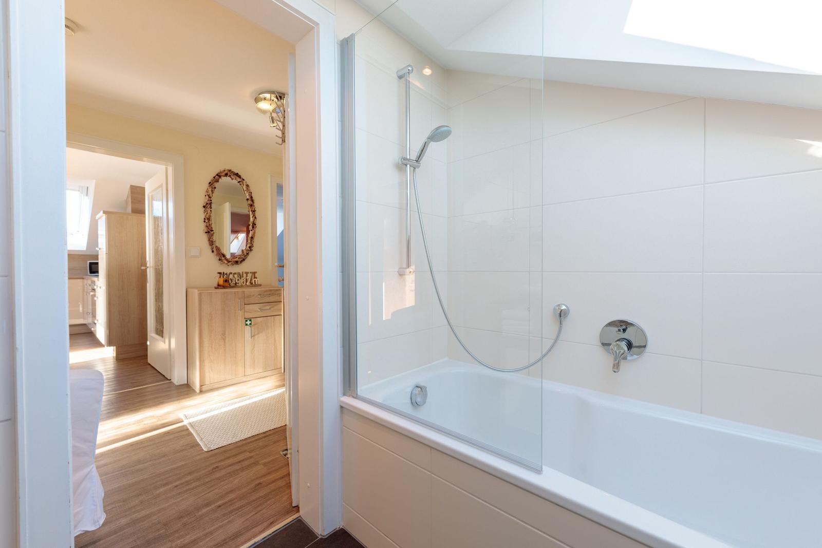 Bad mit Dusche und Badewanne, Blick in Wohnbereich mit Holzboden und Spiegel.