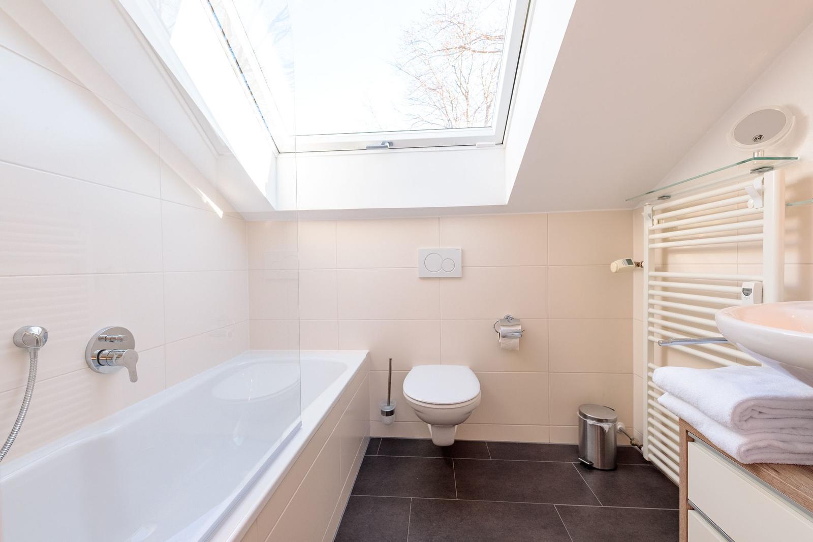 Badezimmer mit Dusche, Toilette und Waschbecken unter Dachfenster.
