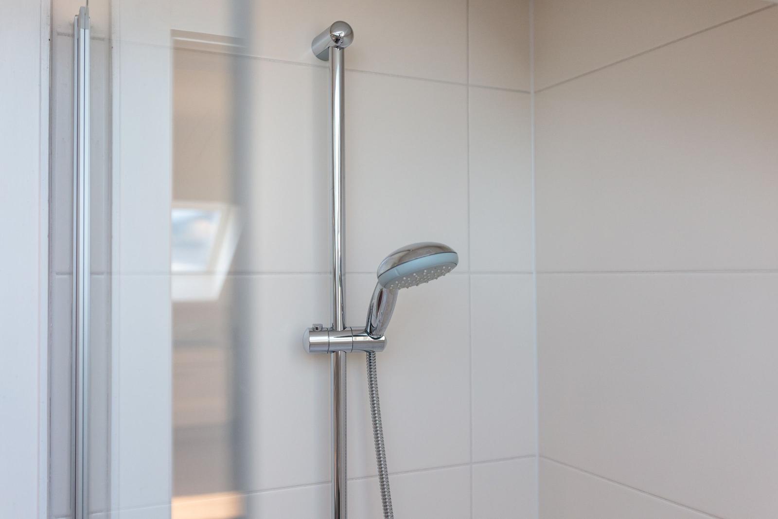 Dusche mit Handbrause und Glaswand in moderner Badewanne.