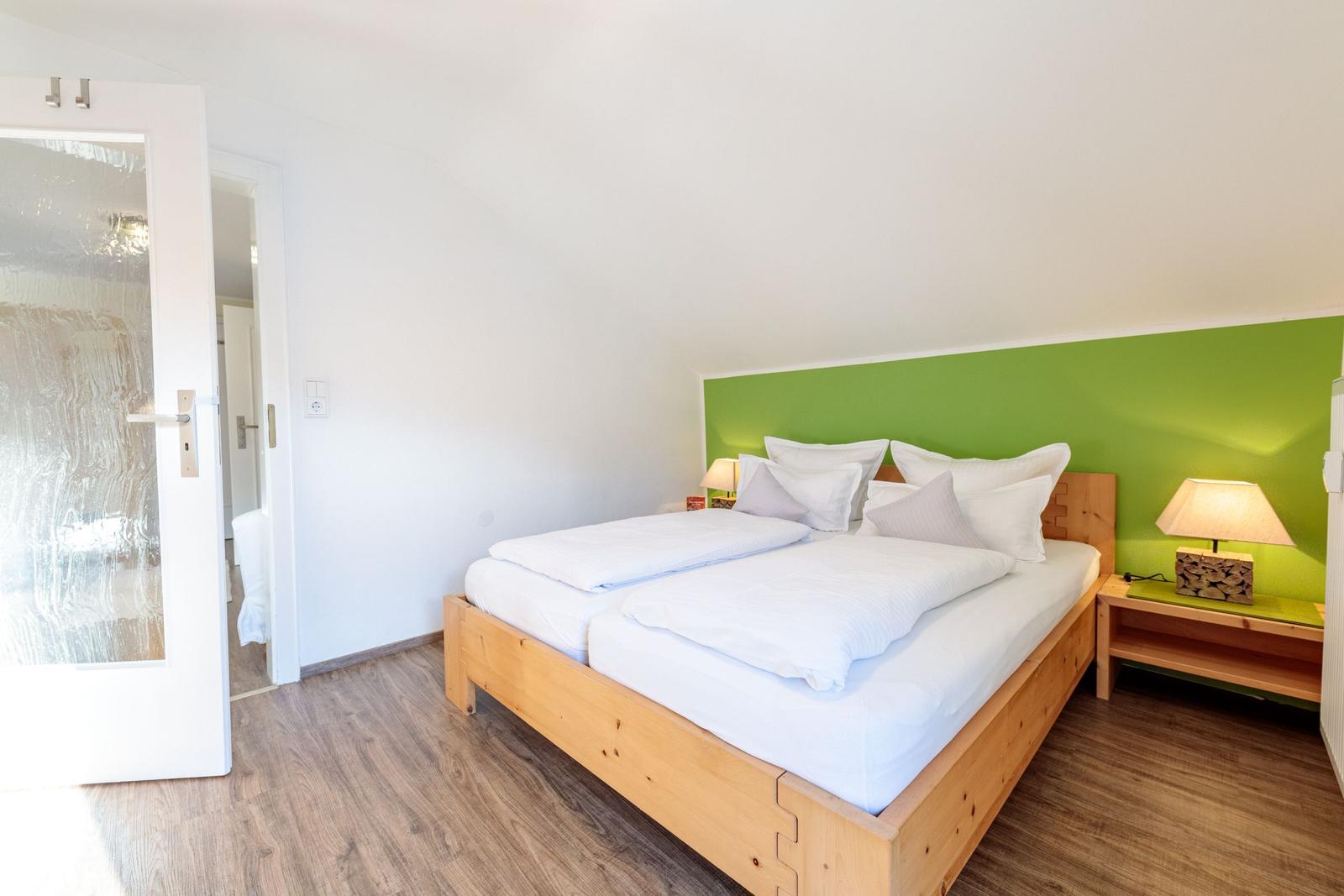 Schlafzimmer mit Doppelbett, grüner Wand und Holzmöbel.