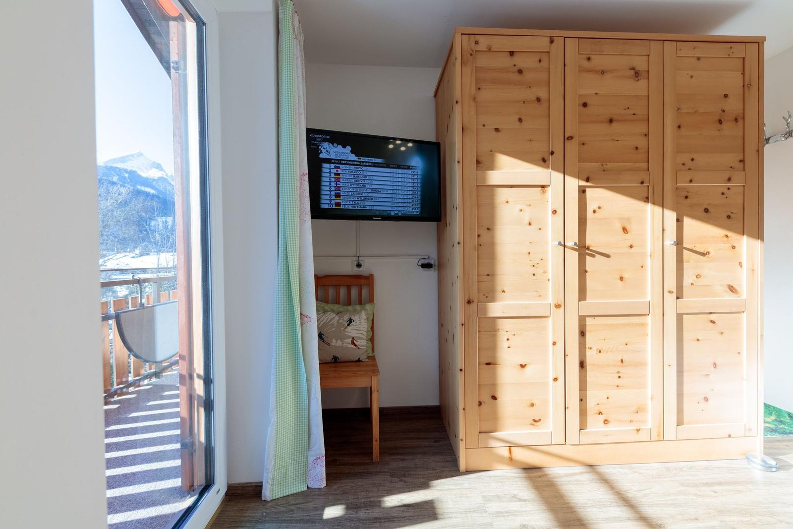 Ein Zimmer mit Holzschrank, Fernseher und Balkonblick auf Berge.