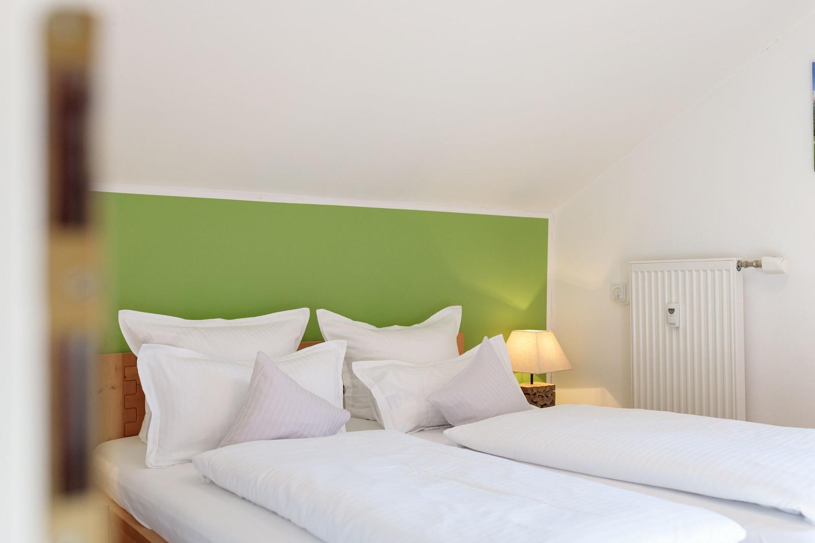 Schlafzimmer mit Doppelbett, grüner Wand und Nachttisch mit Lampe.