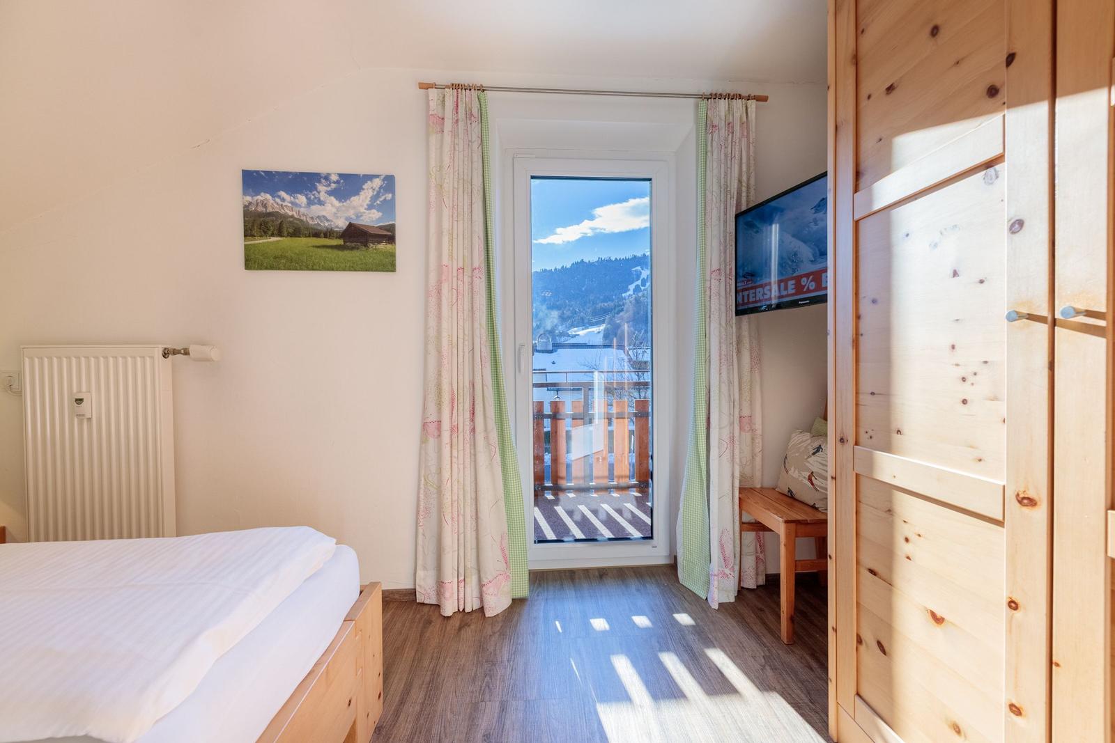 Schlafzimmer mit Balkon, TV und Holzmöbel.