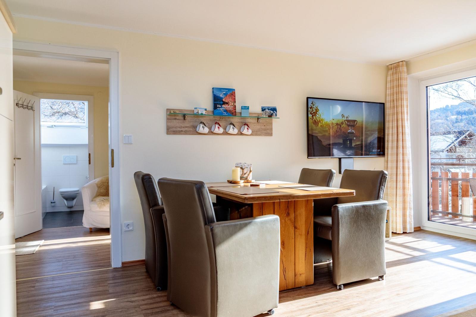 Esszimmer mit Holztisch, Stühlen und Fernseher. Durchgang zur Toilette und Balkon.