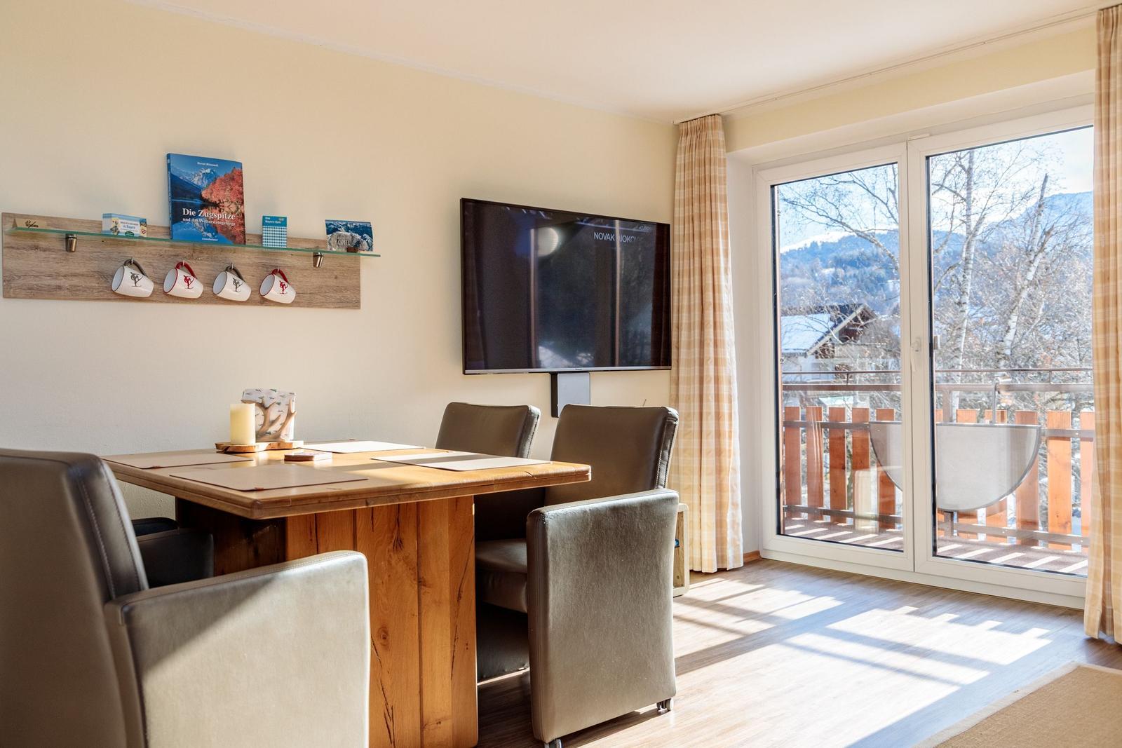 Esszimmer mit Holztisch, Stühlen und TV. Balkon mit Blick auf Berge.