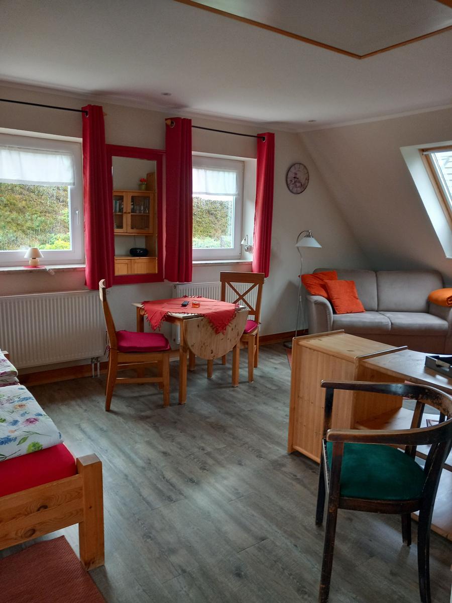 Wohnraum mit Sofa, Esstisch und Fenstern mit roten Vorhängen.