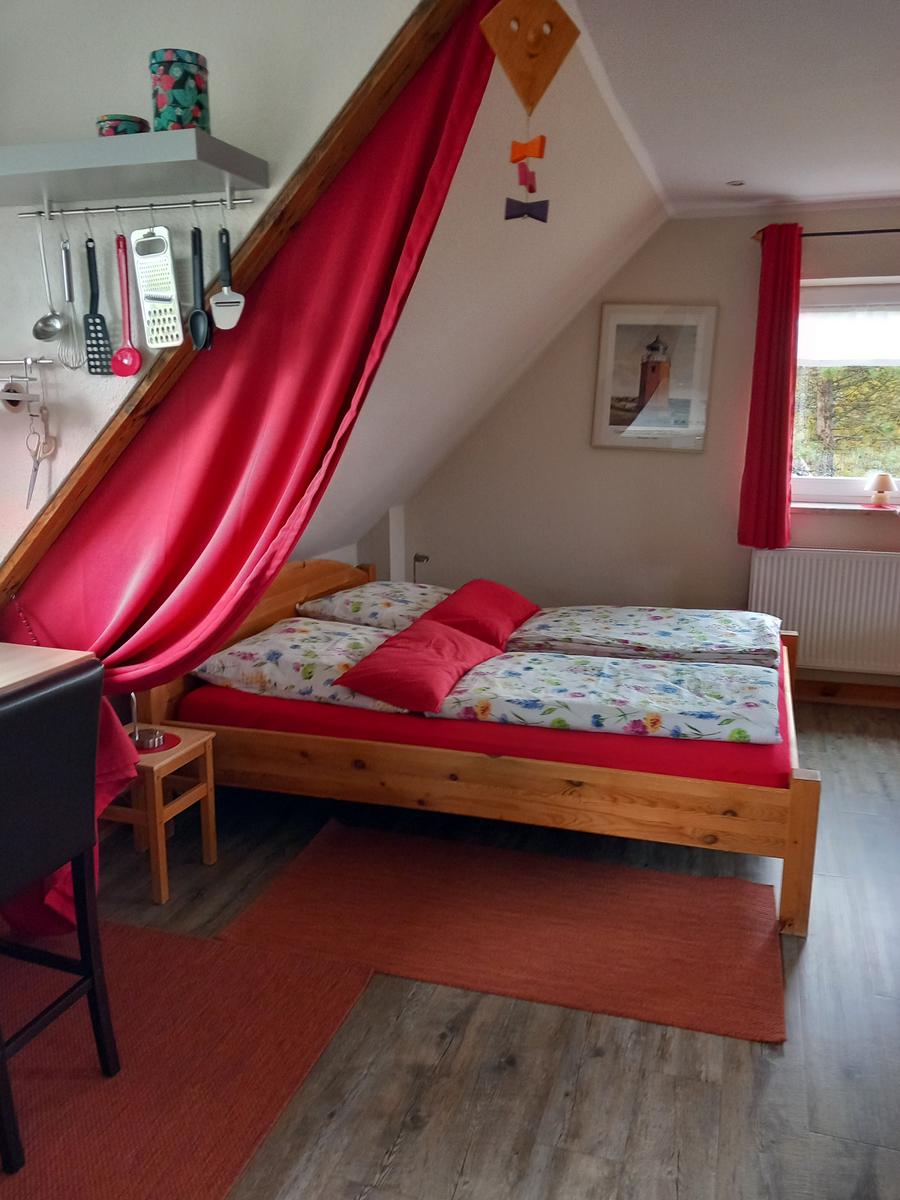 Schlafzimmer mit Dachschräge, roter Vorhang, Holzbett und Fenster mit Blick.