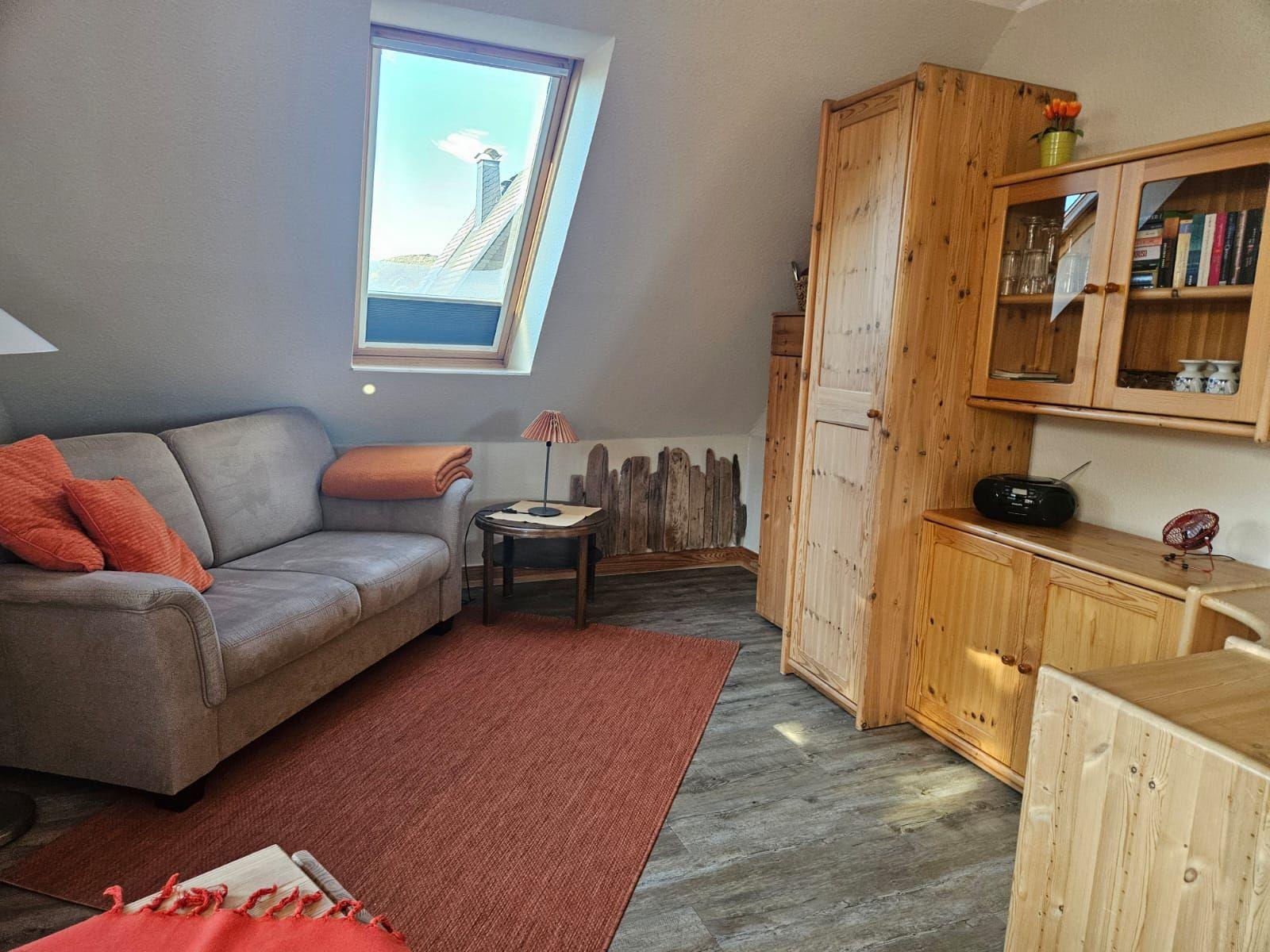 Wohnraum mit Sofa, Holzmöbeln und Dachfenster. Teppich und Kissen in Rot.