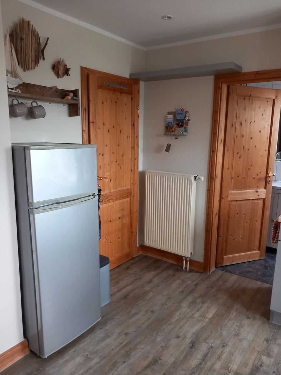 Küche mit Kühlschrank, Holztüren und Heizkörper an der Wand.
