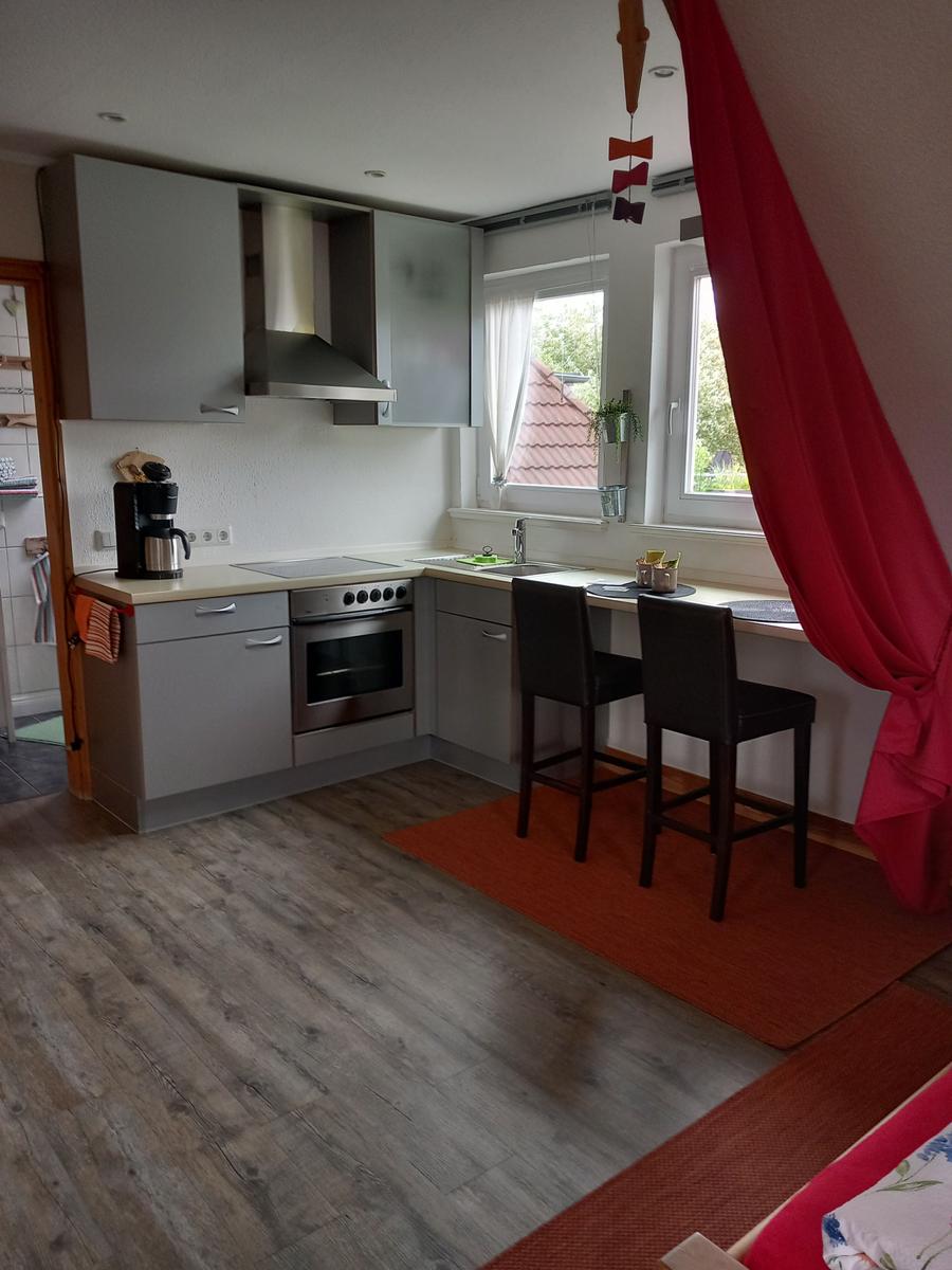 Küche mit Arbeitsplatte, Herd und Fenster. Zwei Barhocker stehen auf Teppich.