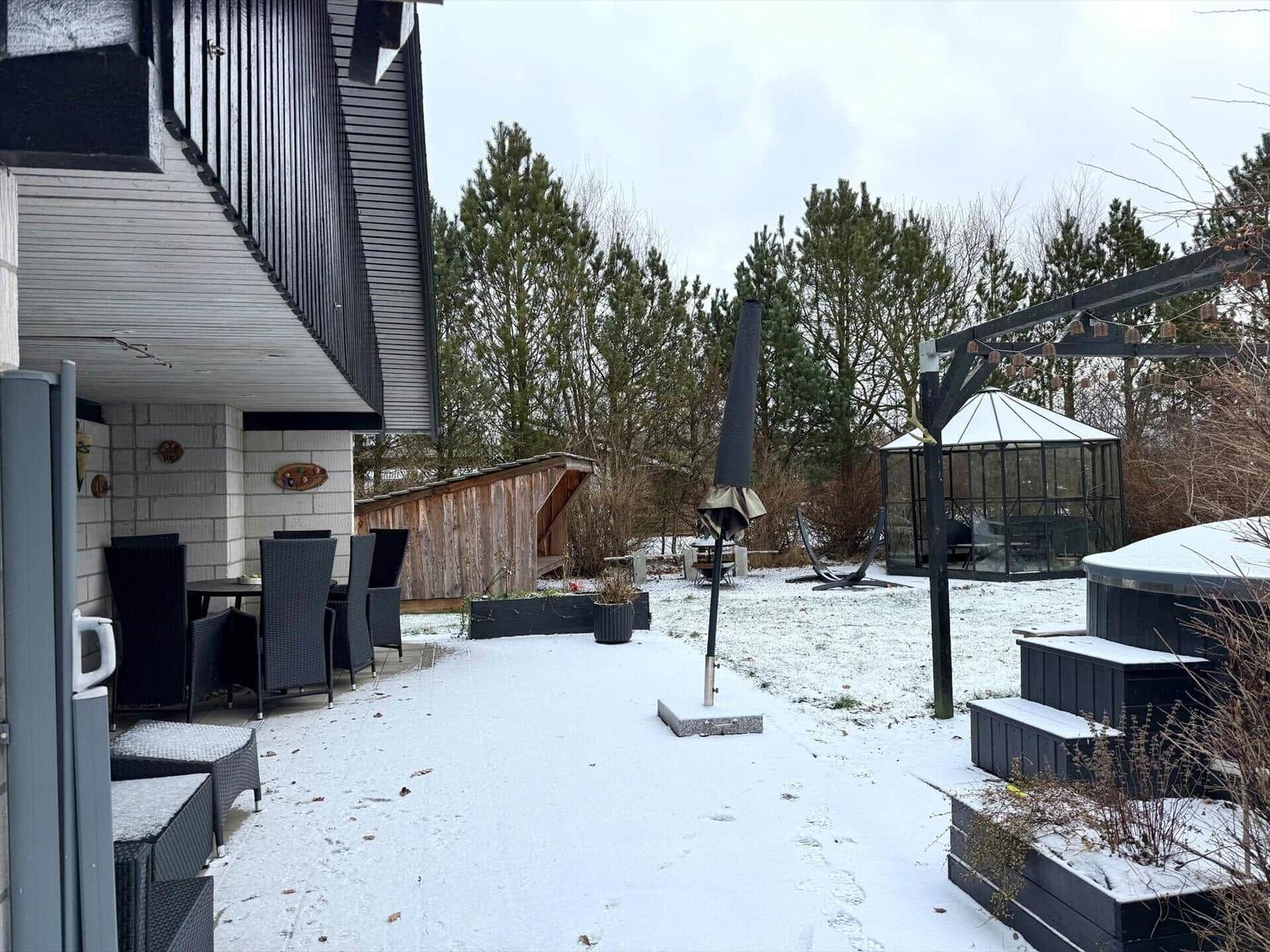 Schneebedeckter Garten mit Terrasse, Sonnenschirm und Whirlpool.