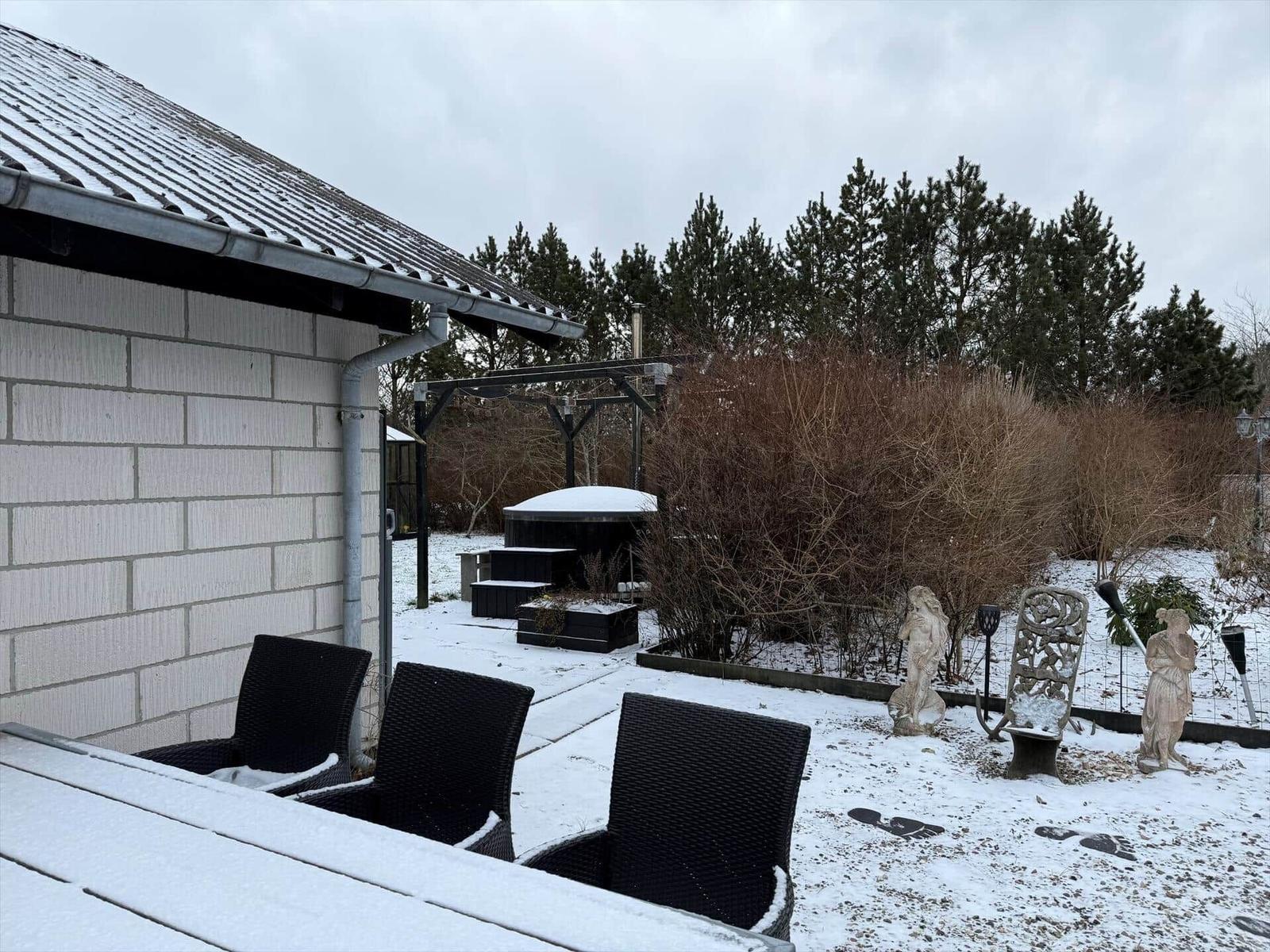 Schneebedeckter Garten mit Sitzgelegenheiten und Statuen. Im Hintergrund sind Bäume und ein Pavillon sichtbar.