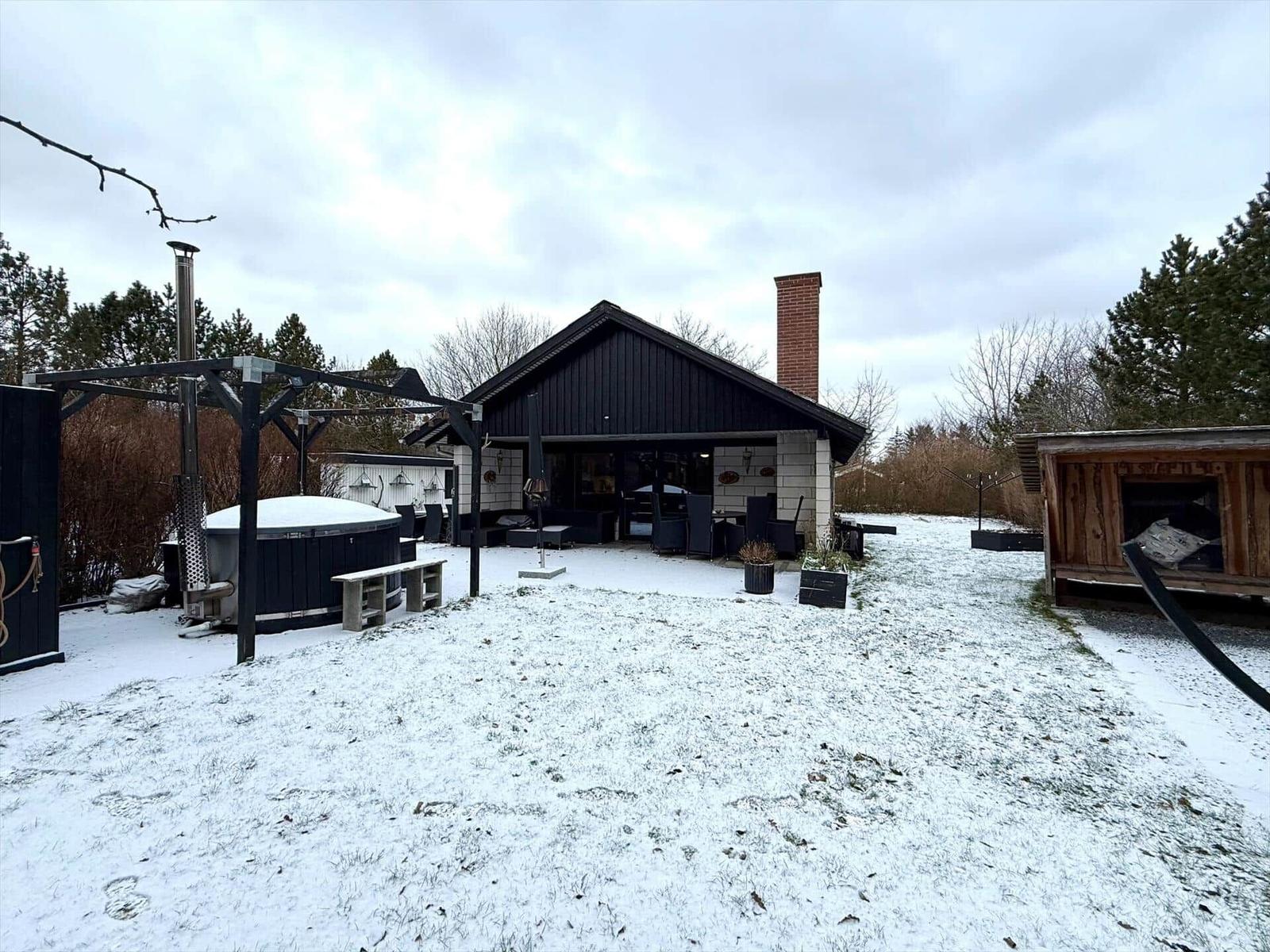 Schwarz lackierte Hütte mit Terrasse und Whirlpool im Schnee.