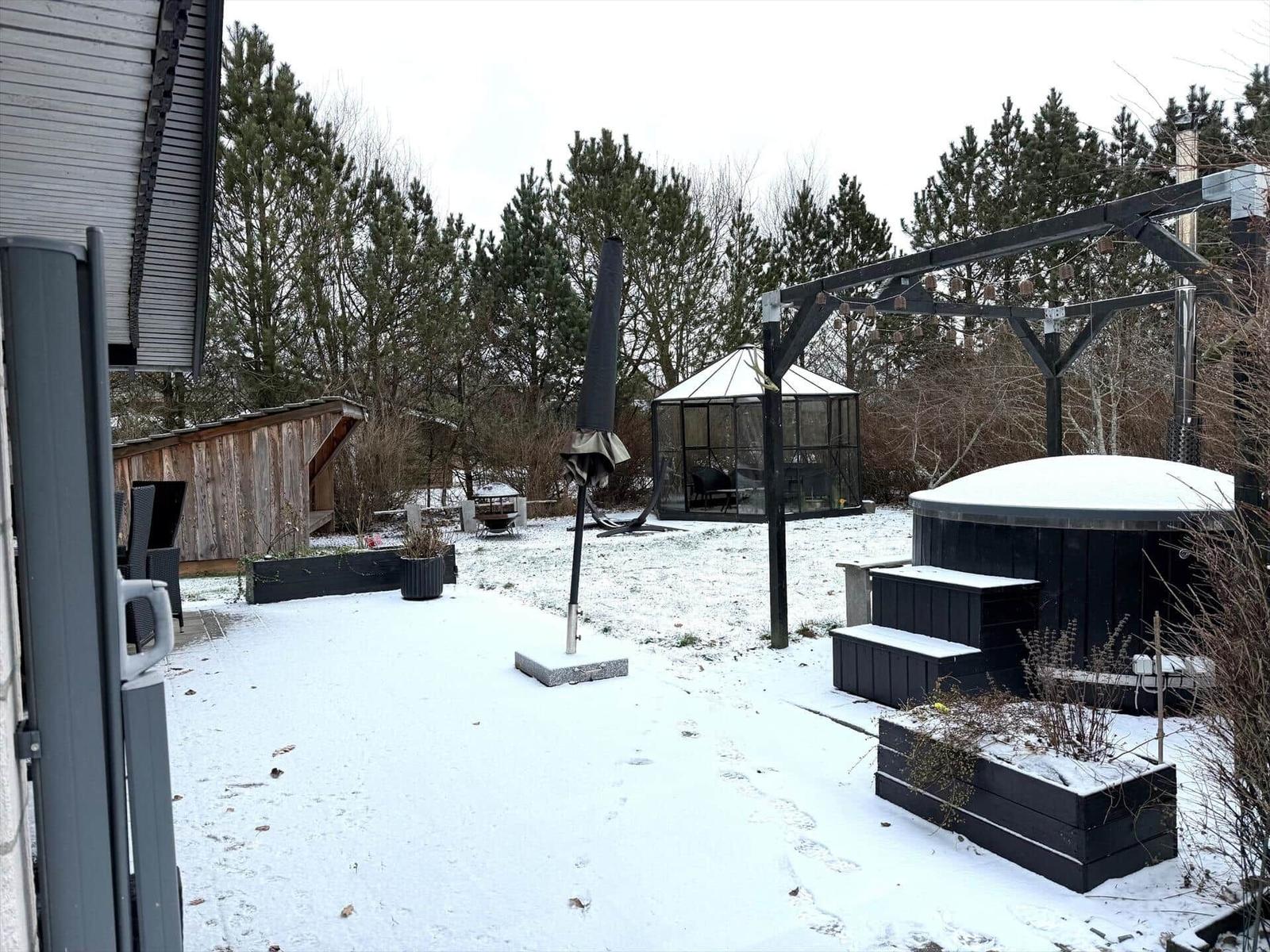 Schneebedeckter Garten mit Whirlpool, Pavillon und Holzhaus.