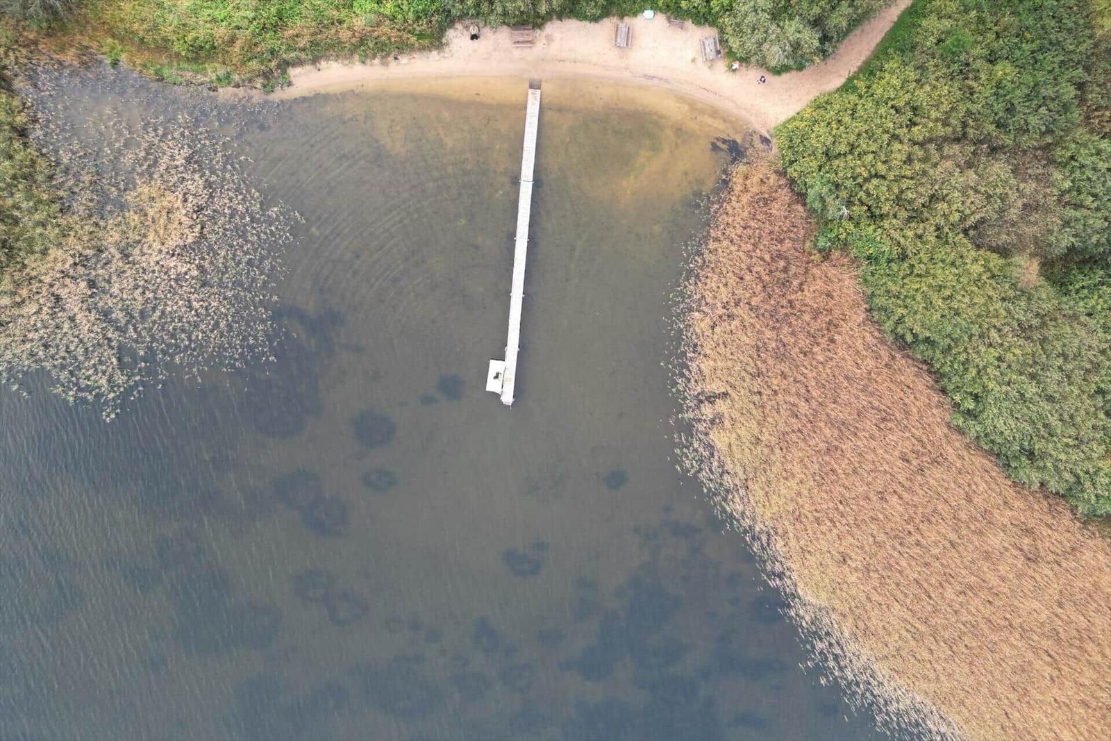 Hafenbecken mit Steg und Strand, umgeben von Vegetation.