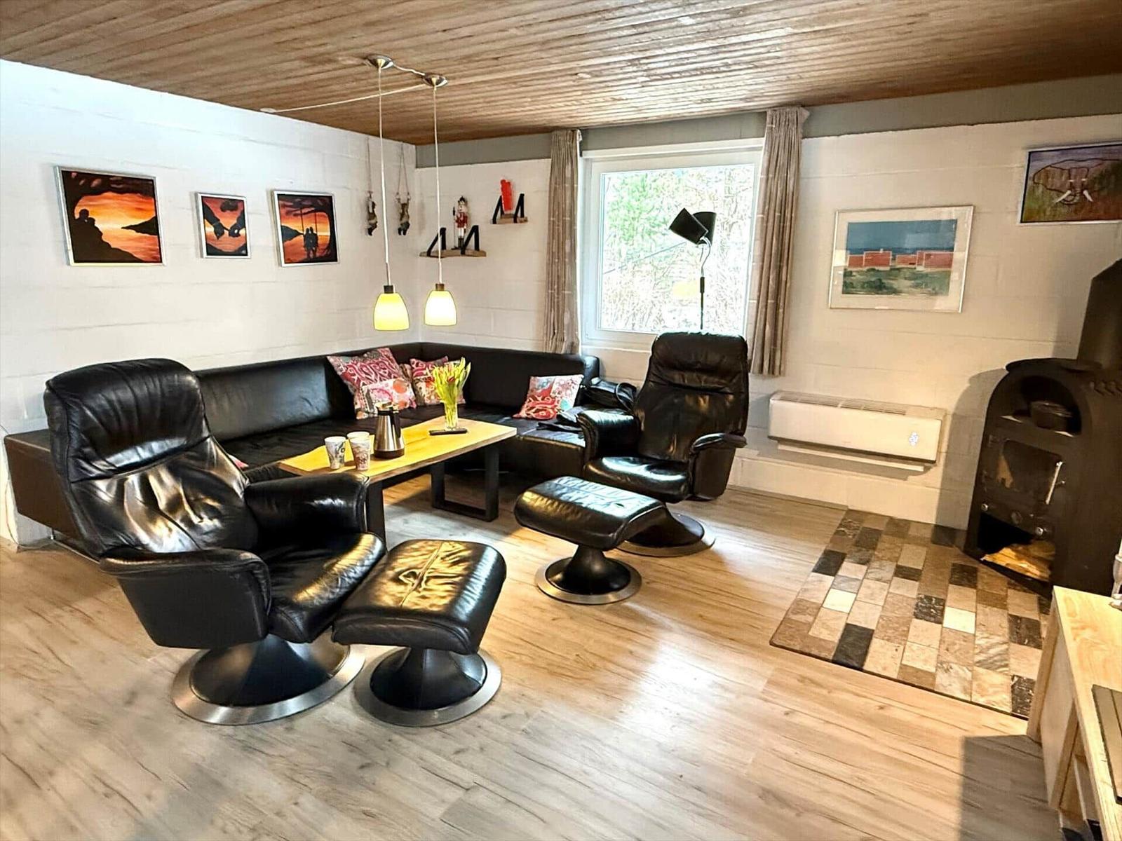 Wohnzimmer mit Ledersofa, zwei Sessel und Kaminofen. Holzfußboden und Wandbilder.