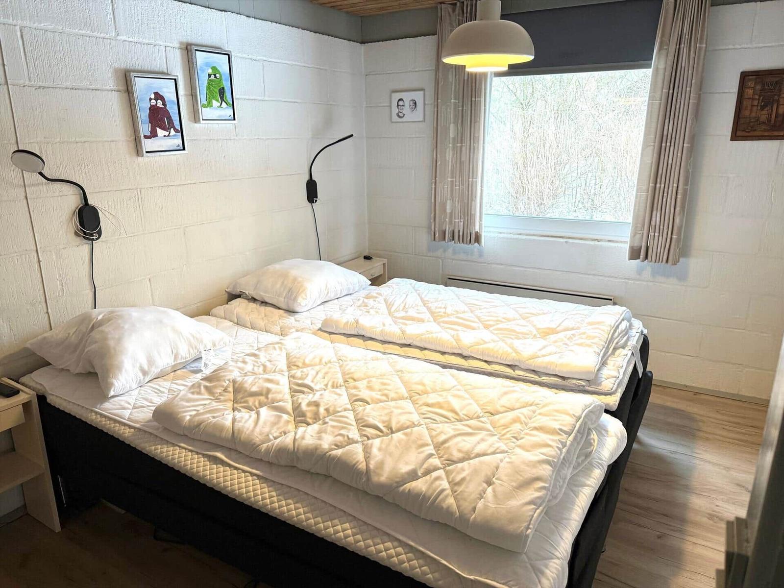 Schlafzimmer mit Bett, Fenster und Wandbildern.