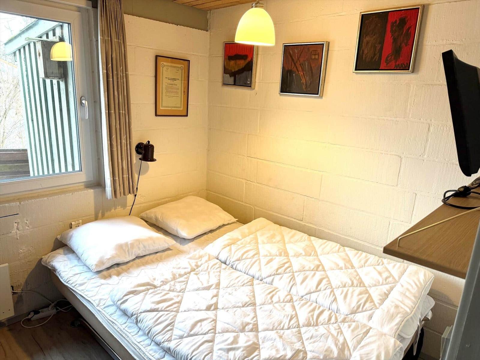Schlafzimmer mit Bett, Wandbildern und Fenster.