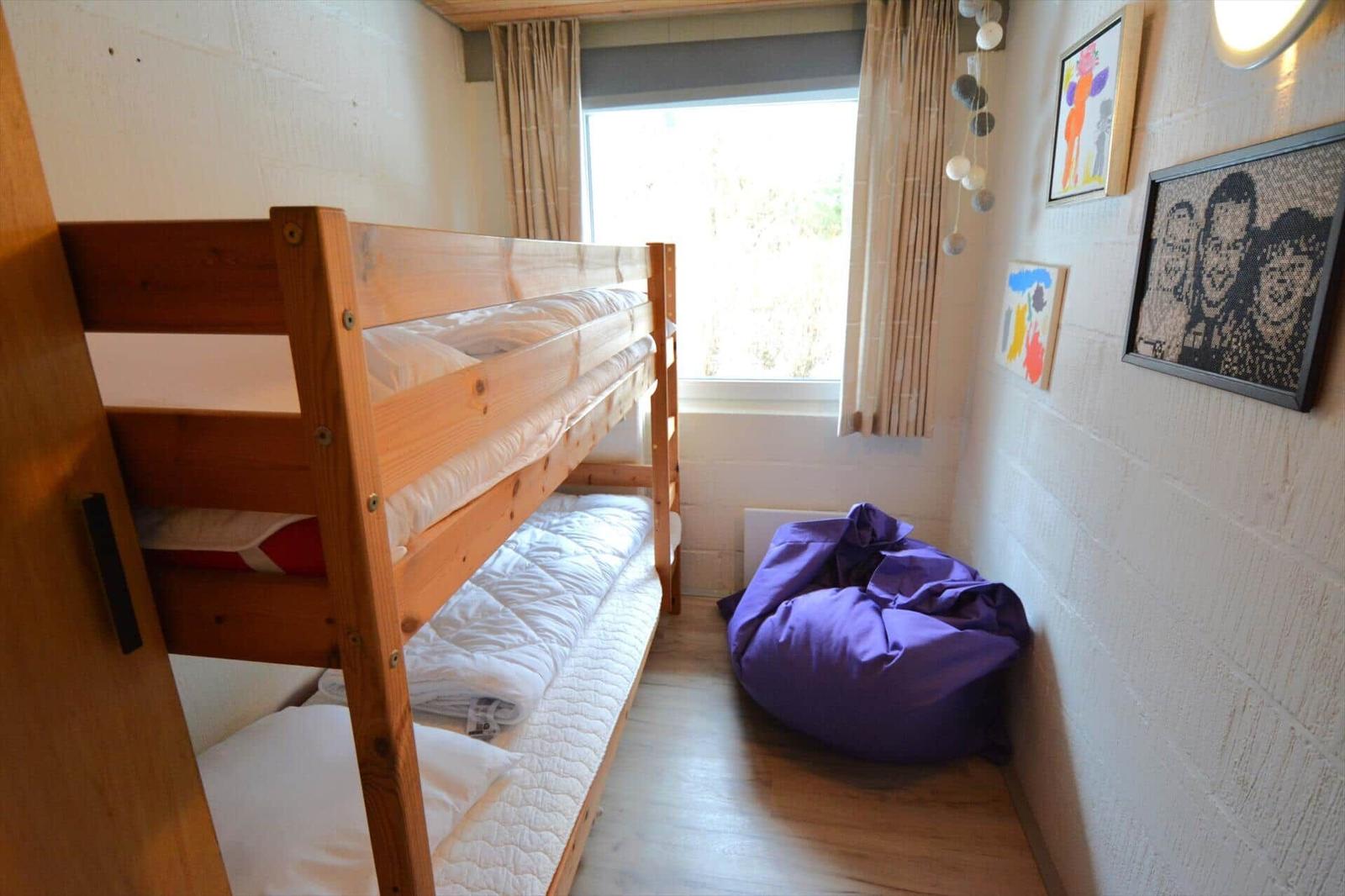 Zimmer mit Holzbett, Fenster und lila Sitzkissen.