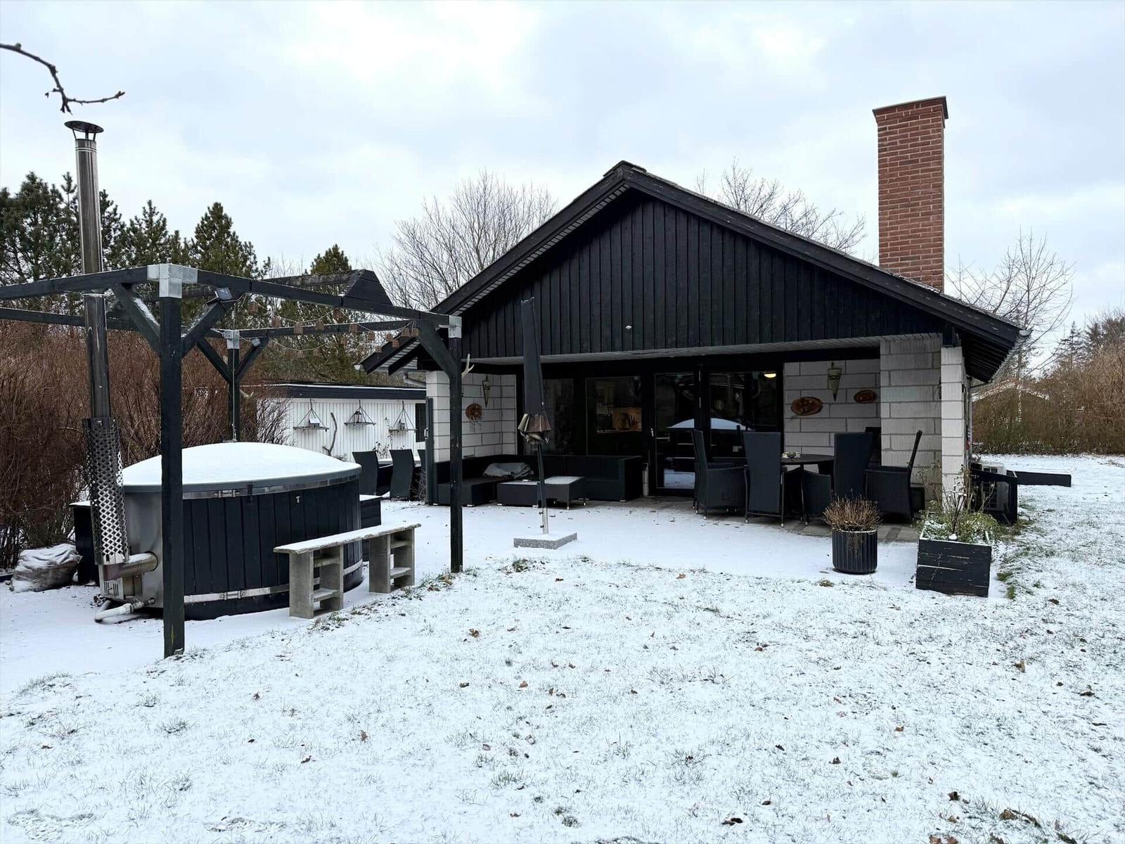 Schwarz lackierte Holzhütte mit Terrasse, Whirlpool und Schneelandschaft.