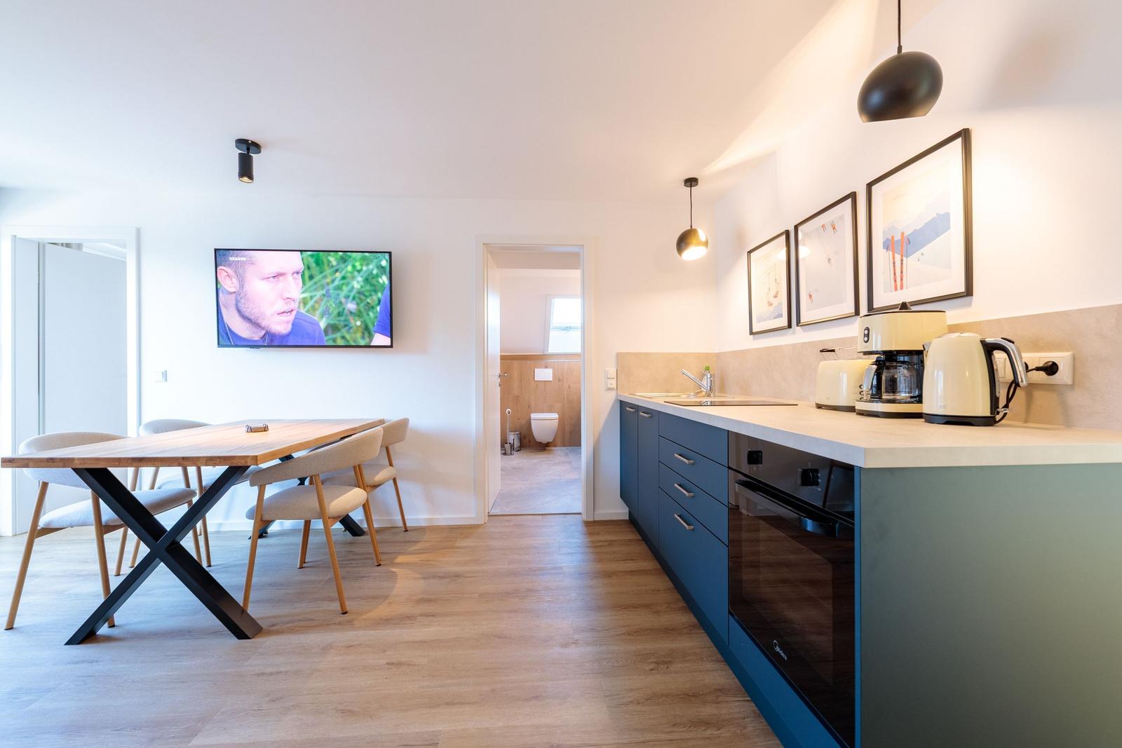 Küche mit Esstisch, TV und Blick in die Toilette.