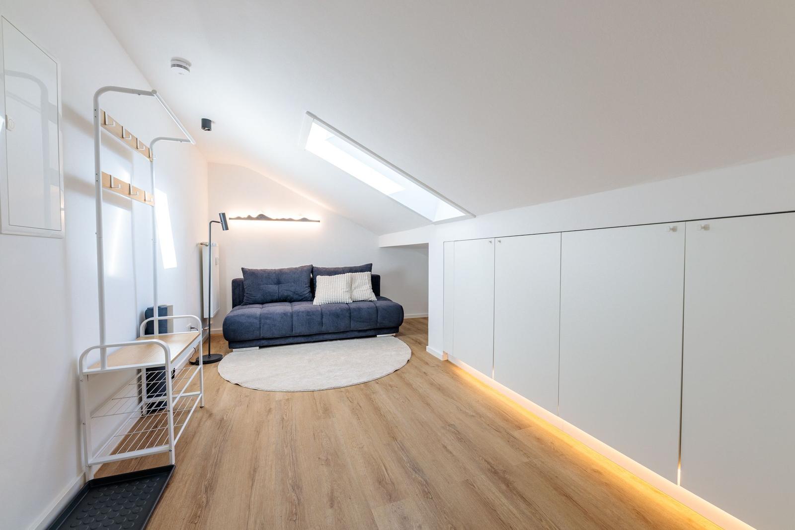 Zimmer mit Sofa, Kleiderständer und Schrank unter Dachschrägen