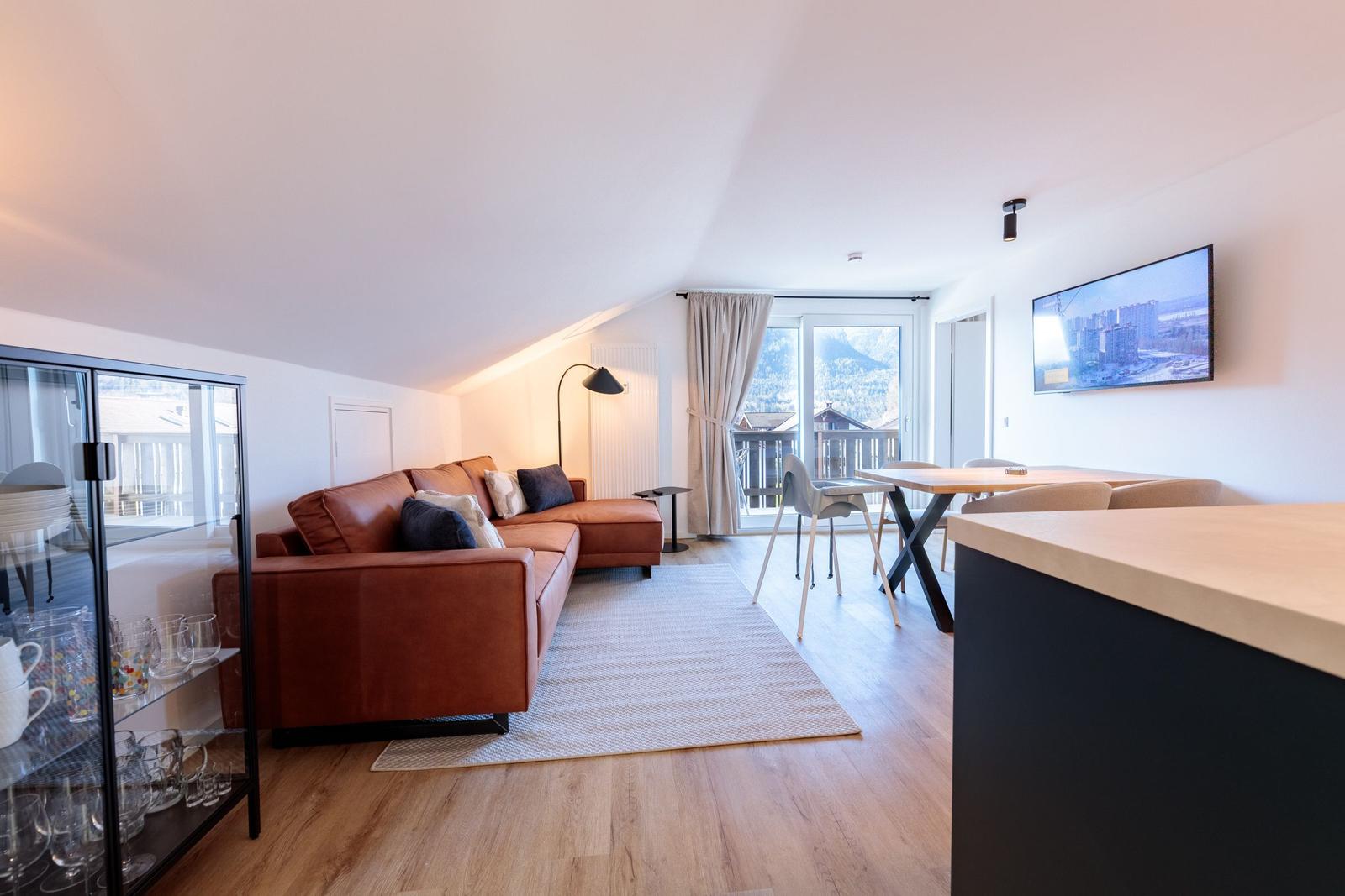 Wohnbereich mit Sofa, Esstisch und TV. Balkon mit Bergblick.
