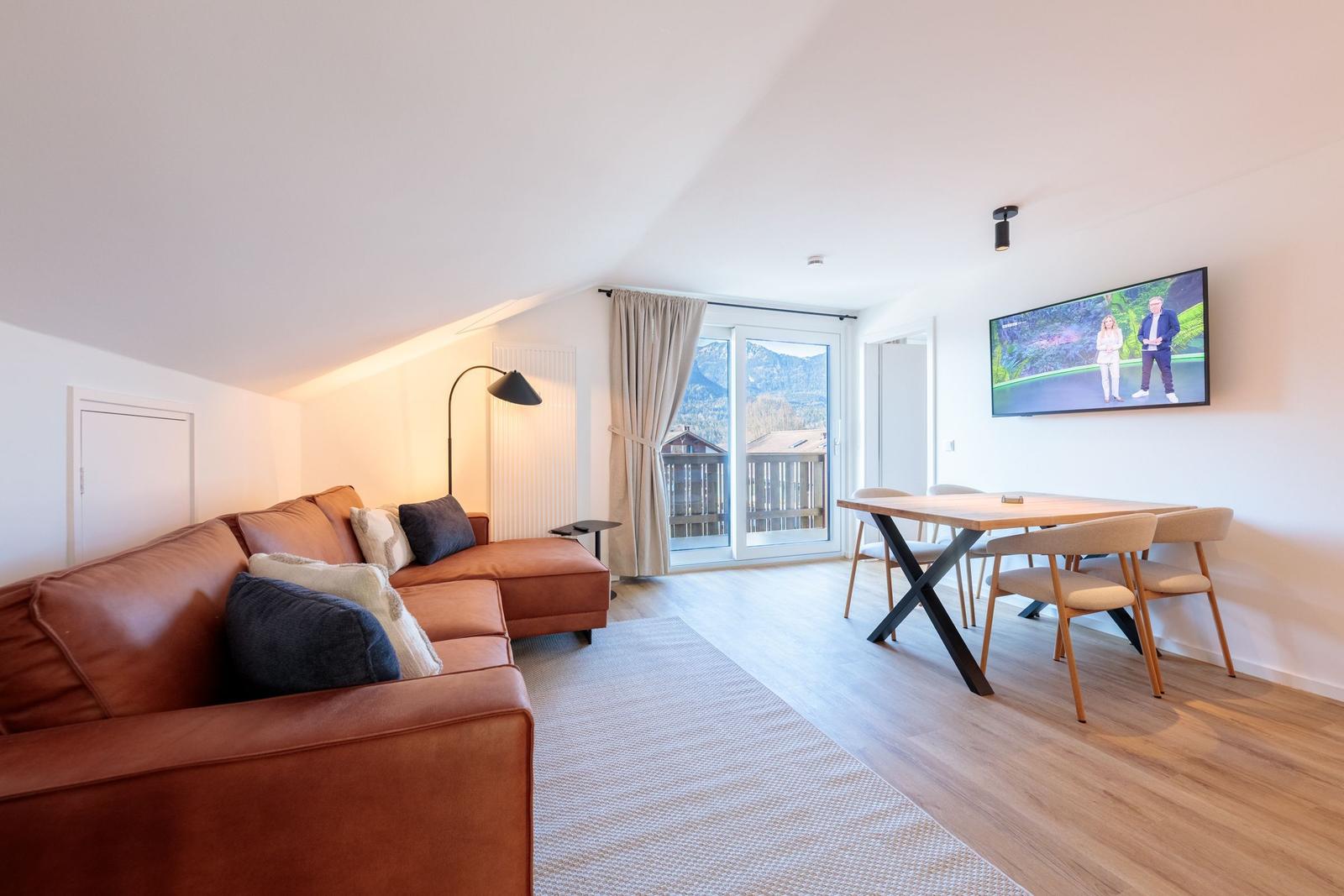 Wohn- und Essbereich mit Sofa, TV und Balkonblick.