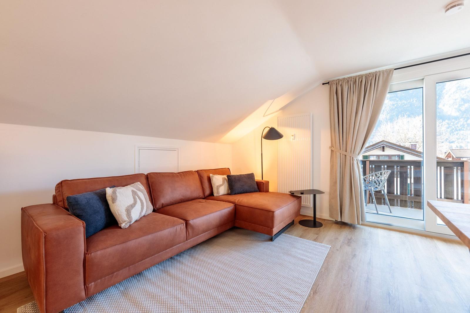 Wohnzimmer mit braunem Sofa, Glasfront und Balkon.