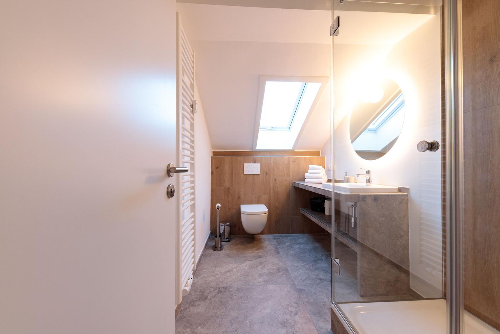 Badezimmer mit Dusche, Waschbecken und Toilette unter Dachschrägen.