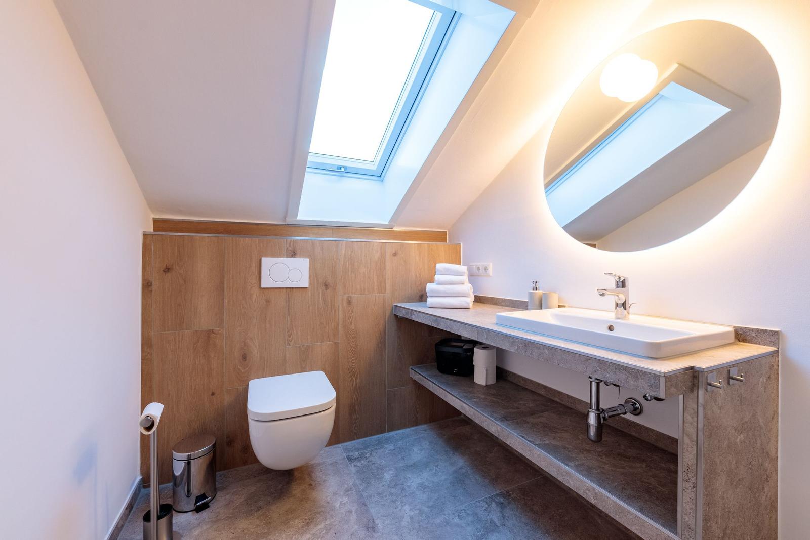 Badezimmer mit Dachschrägen, Waschbecken, Spiegel und Toilette.