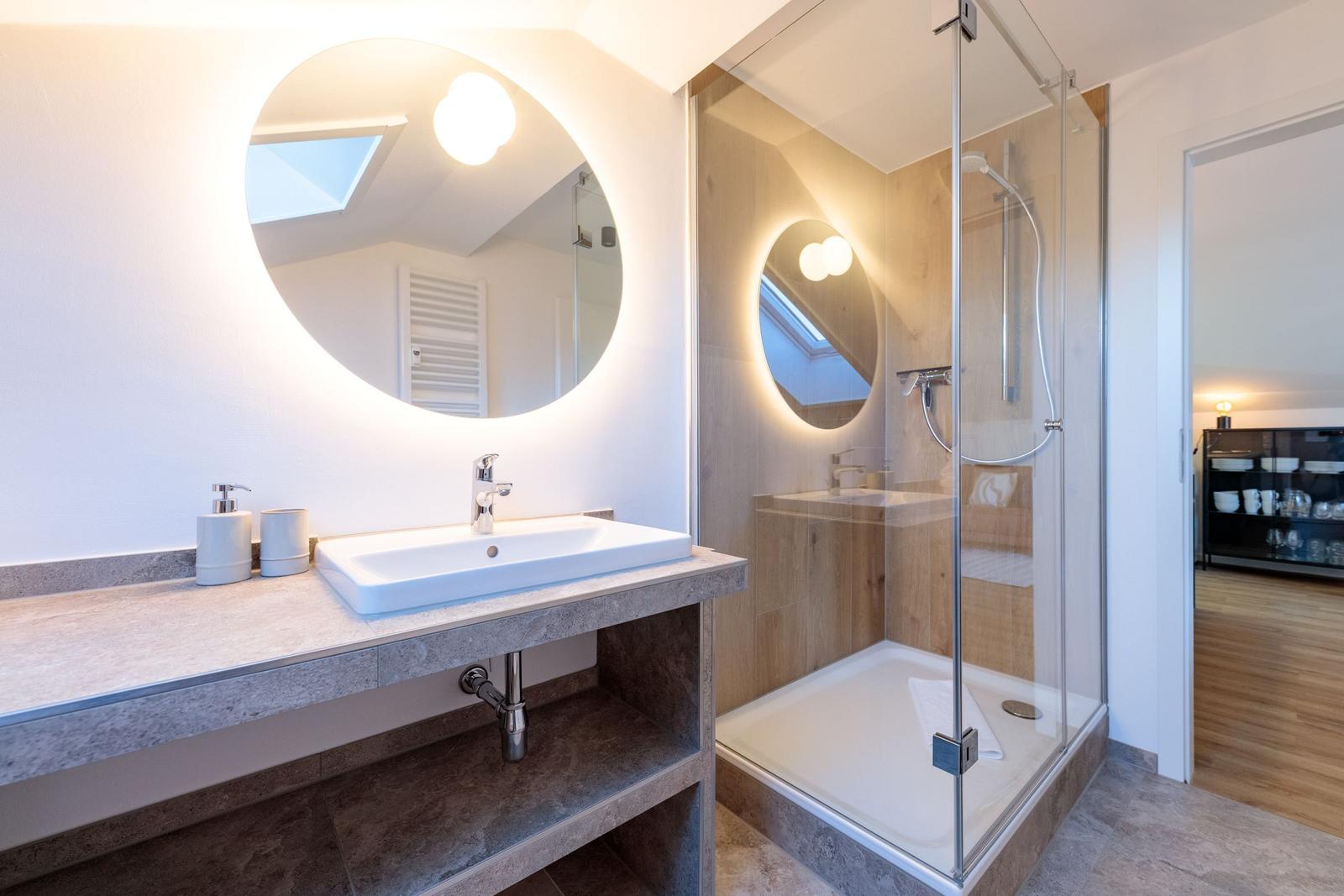 Badezimmer mit Dusche und Waschbecken unter runden Spiegel.