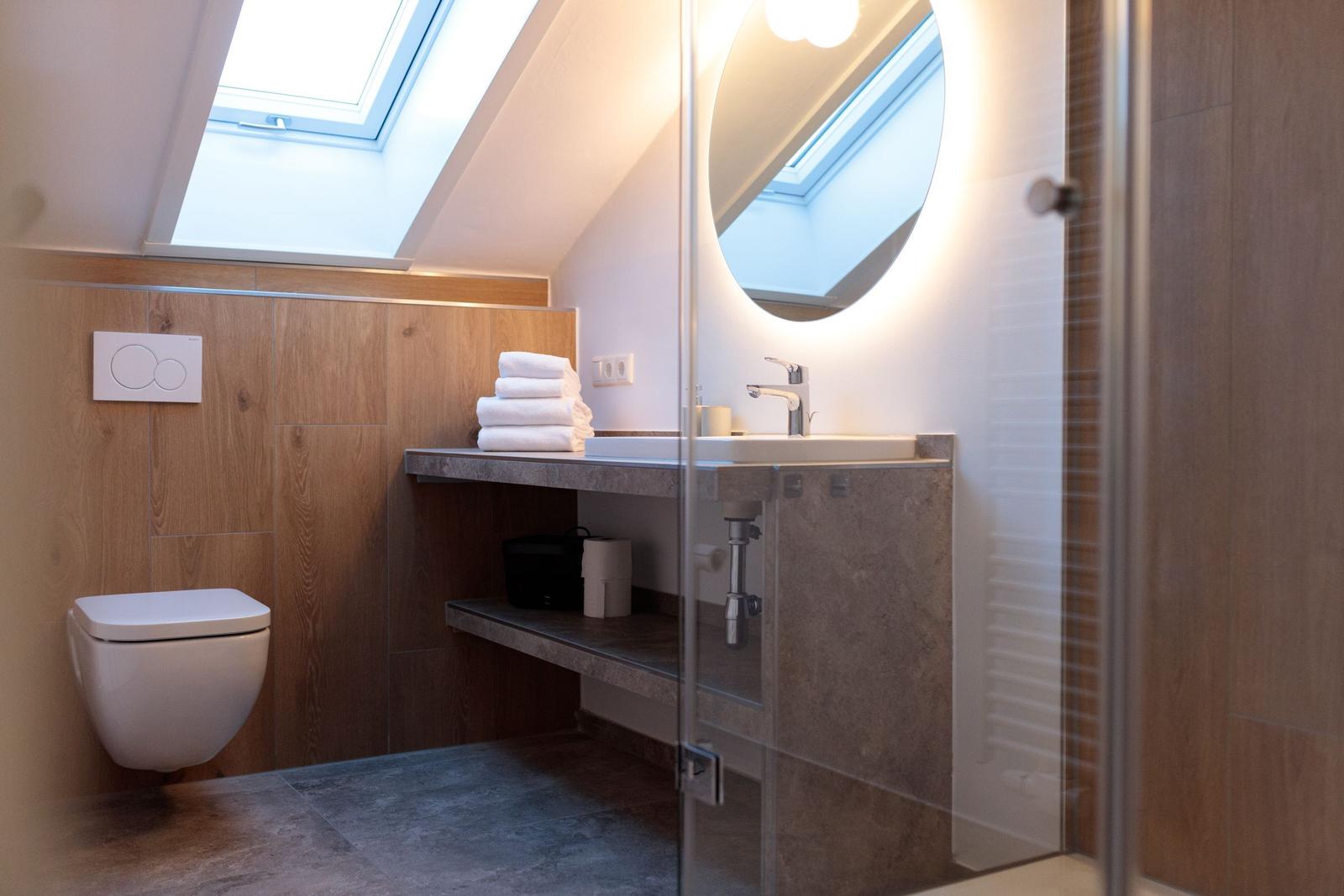 Badezimmer mit Duschabtrennung, Waschbecken und Toilette unter Dachschrägen.