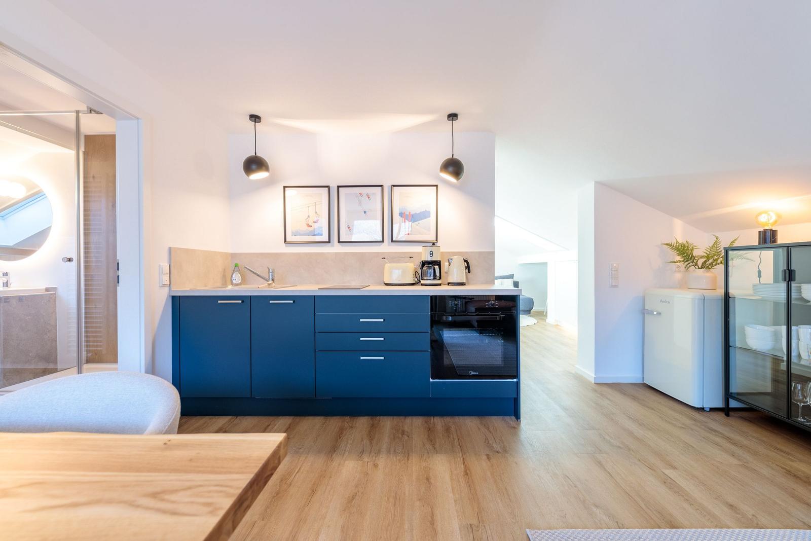 Küche mit blauen Schränken und Holzboden. Im Hintergrund ist ein Wohnbereich.