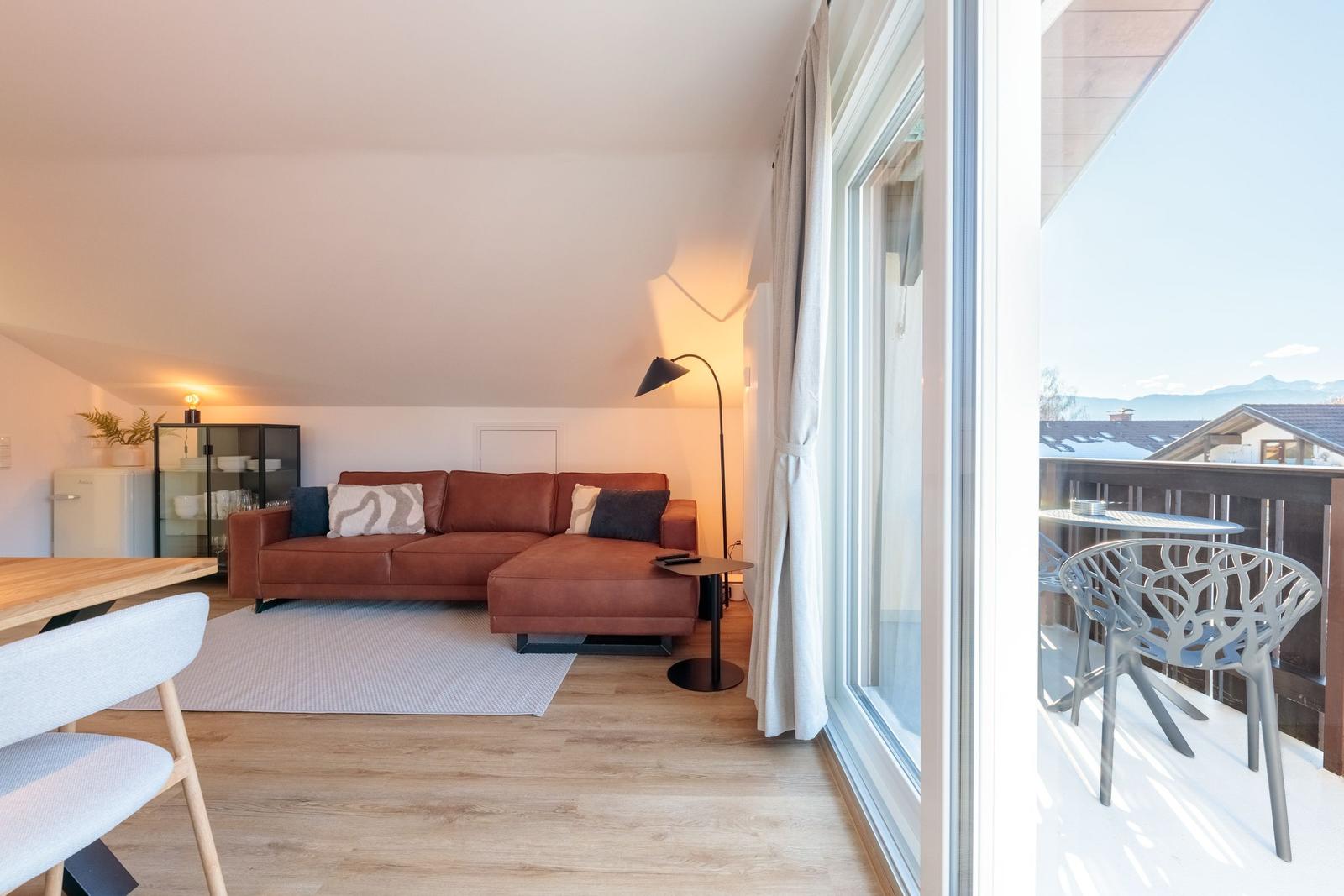 Wohnzimmer mit braunem Sofa, Balkon und Blick auf Berge.