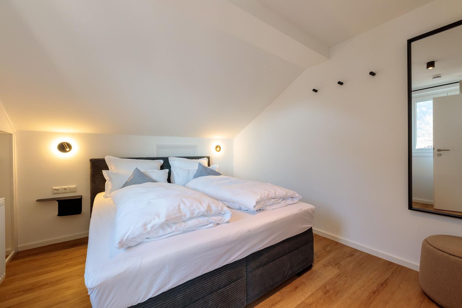 Schlafzimmer mit Doppelbett, Spiegel und Holzboden.