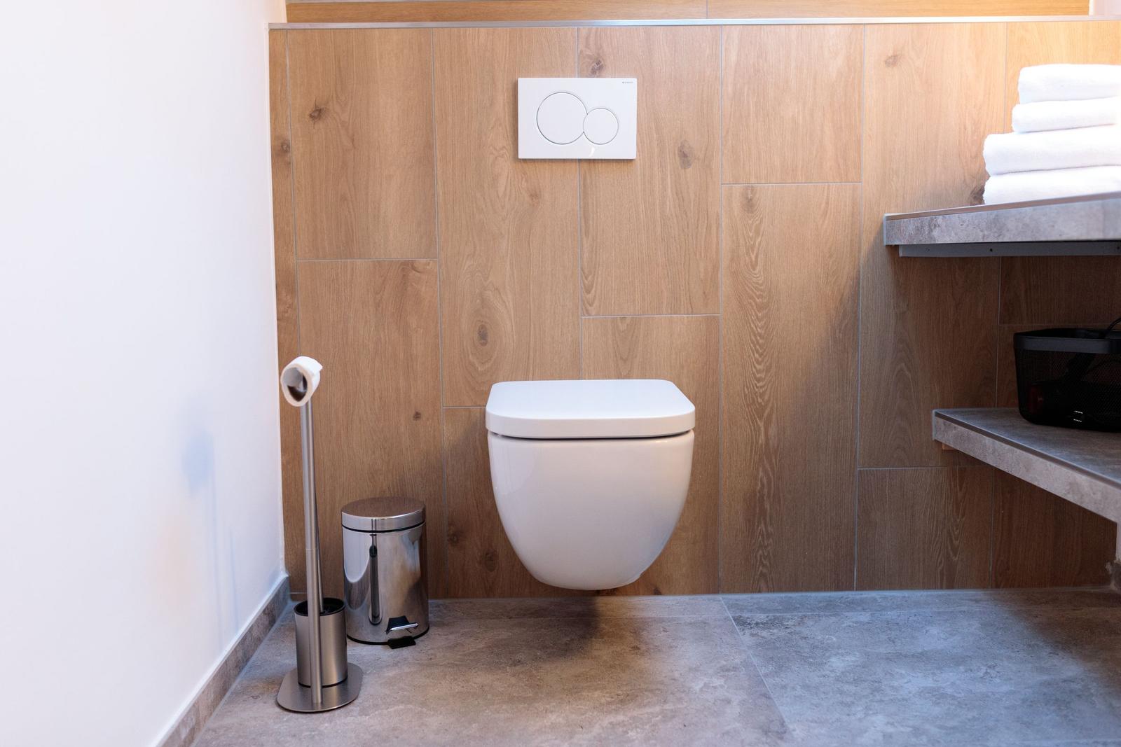 Hängendes WC mit Wandbedienung, Holzwand und Handtüchern auf Regal