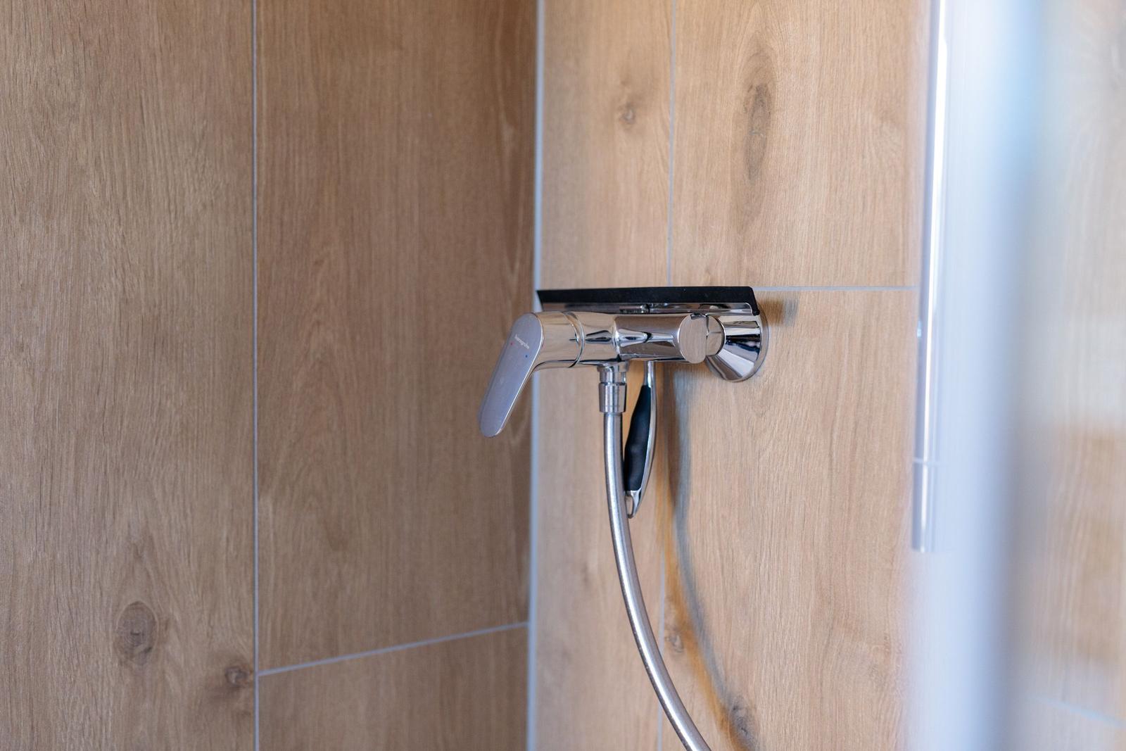 Duschbrause mit Handbrause und Chromarmatur an Holzfliesenwand.