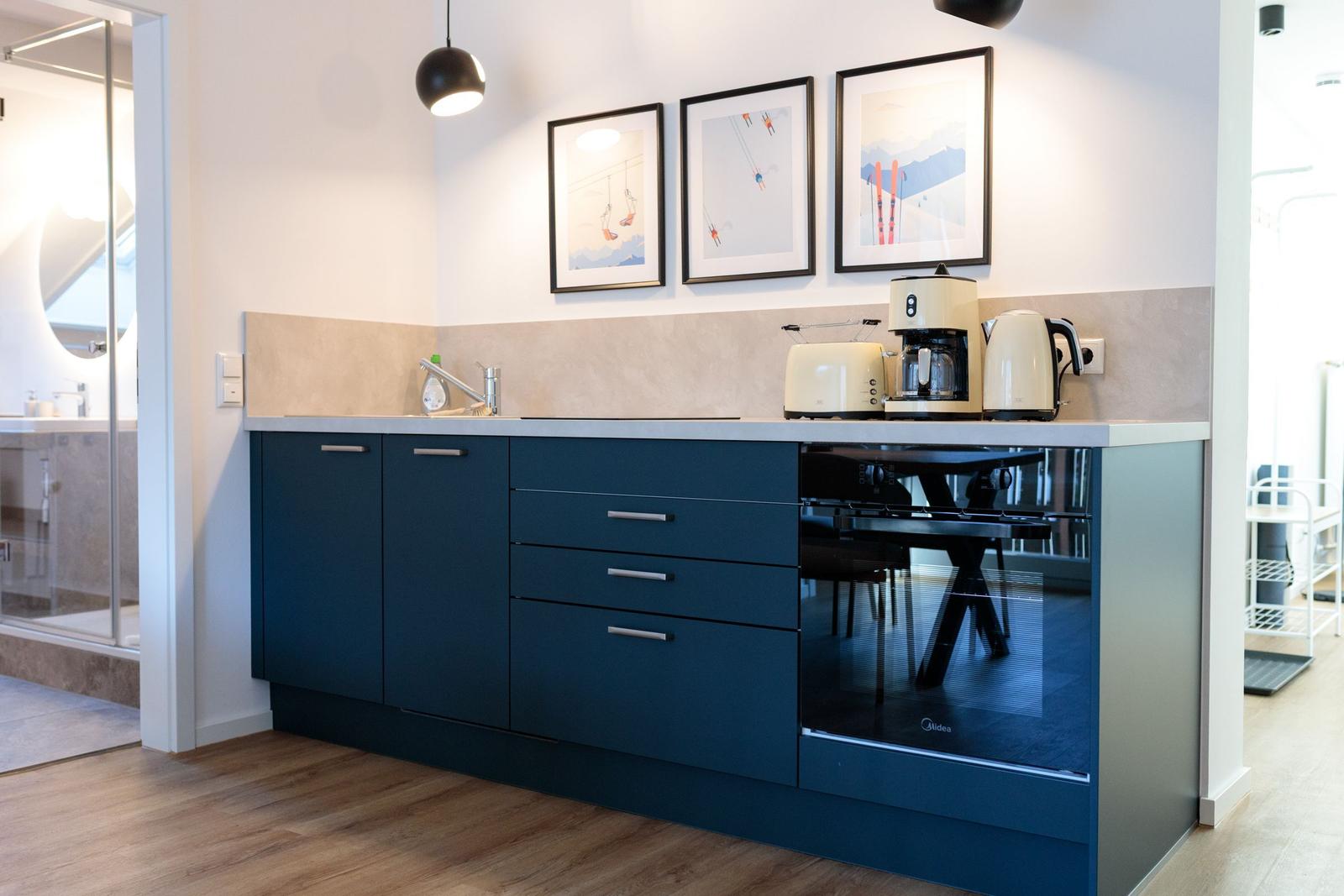 Küche mit blauen Schränken, Kaffeemaschine und Skiaufdrucken an der Wand.