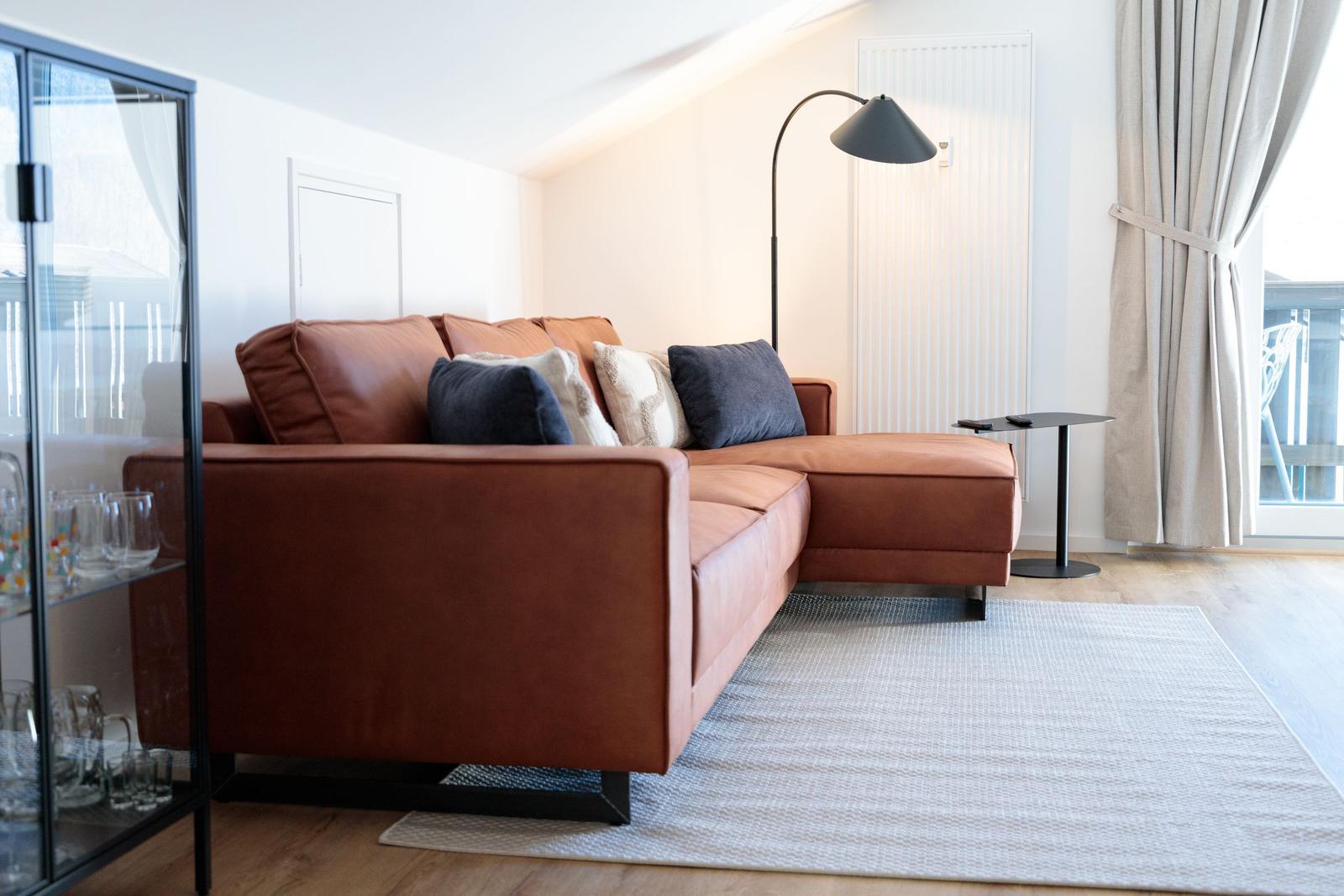 Ein Wohnzimmer mit braunem Sofa, Teppich und Stehlampe.
