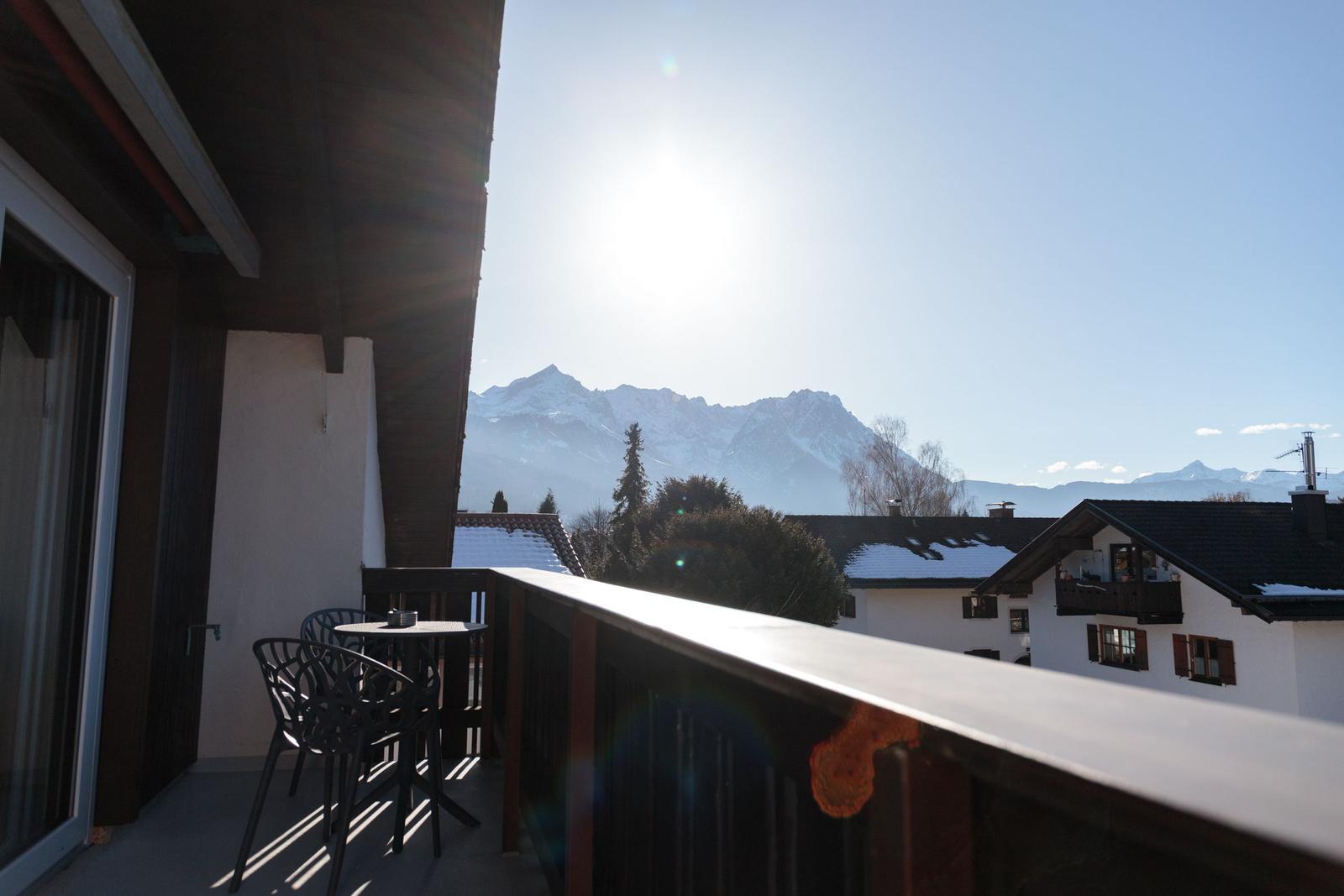 Terrasse mit Tisch und Stühlen, Blick auf schneebedeckte Berge und Dächer.
