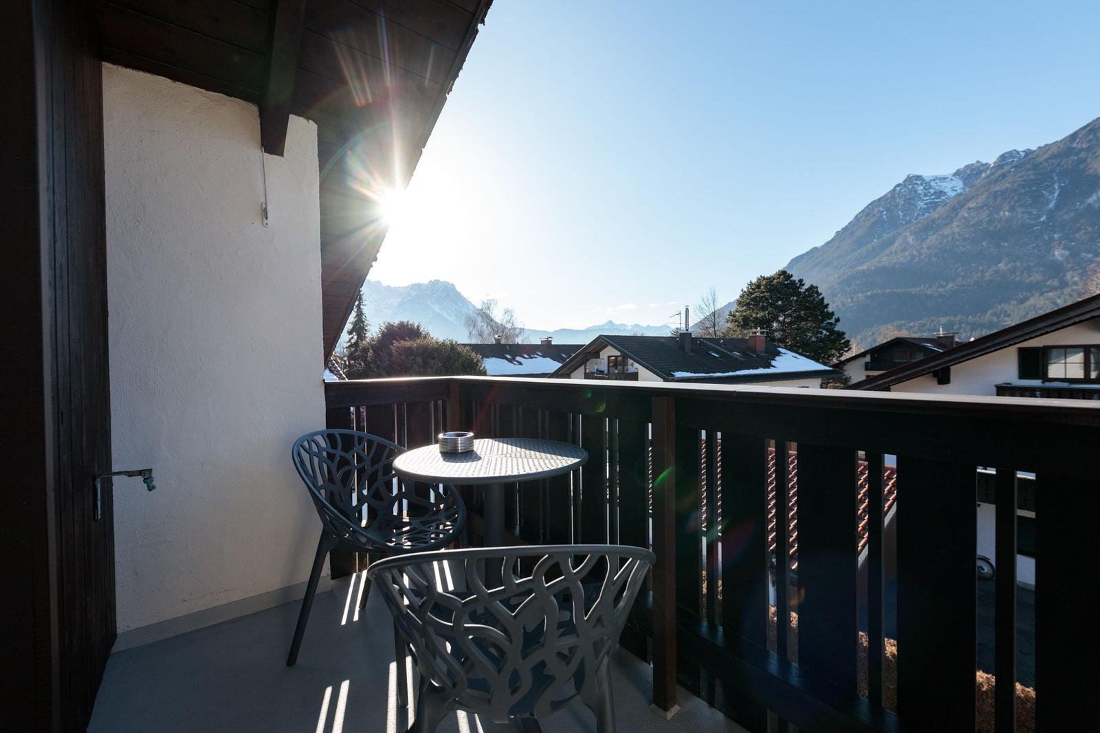 Balcony with table and chairs overlooking snowy mountains and rooftops.