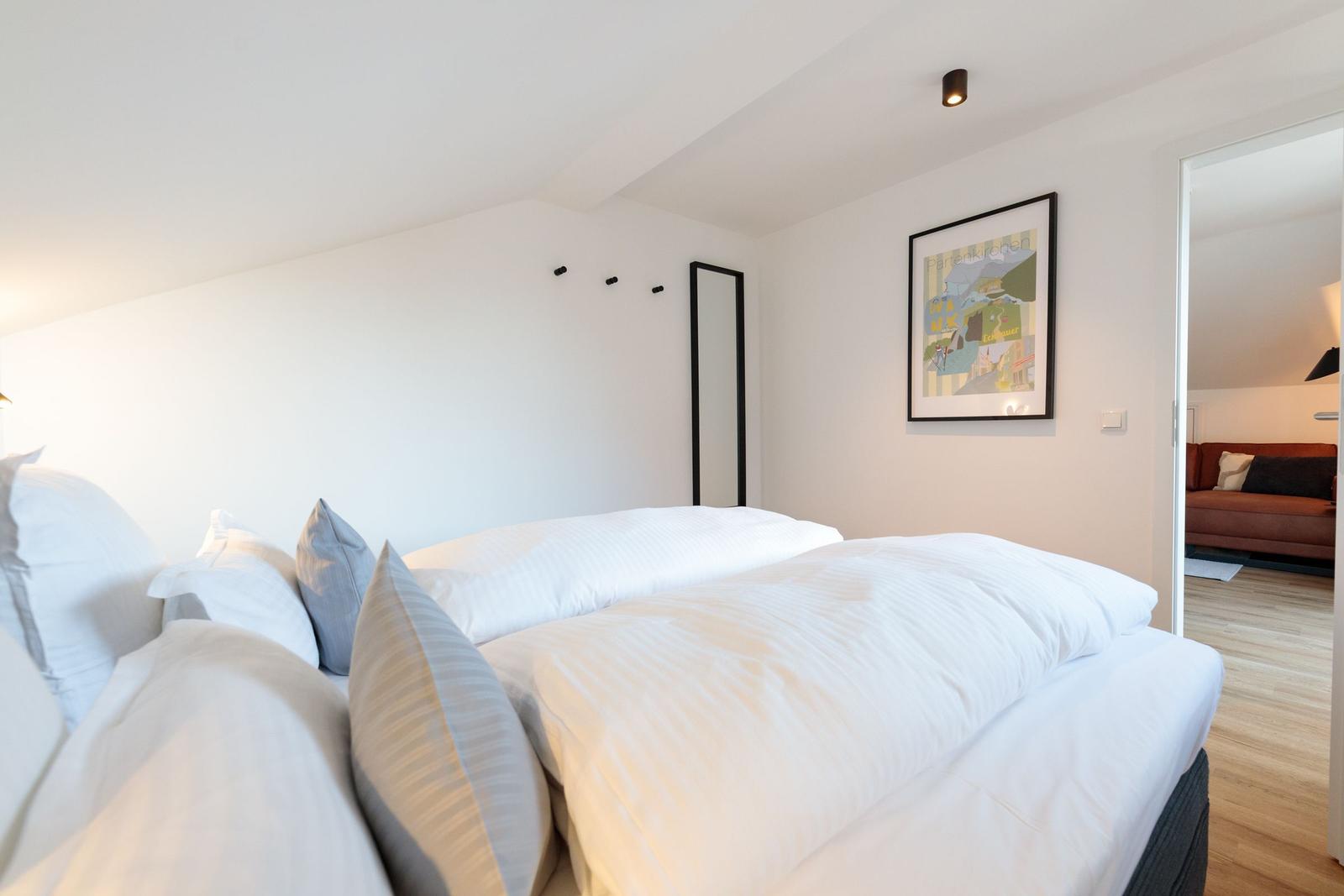 Schlafzimmer mit Bett, Wandbild und Tür zum Wohnbereich.