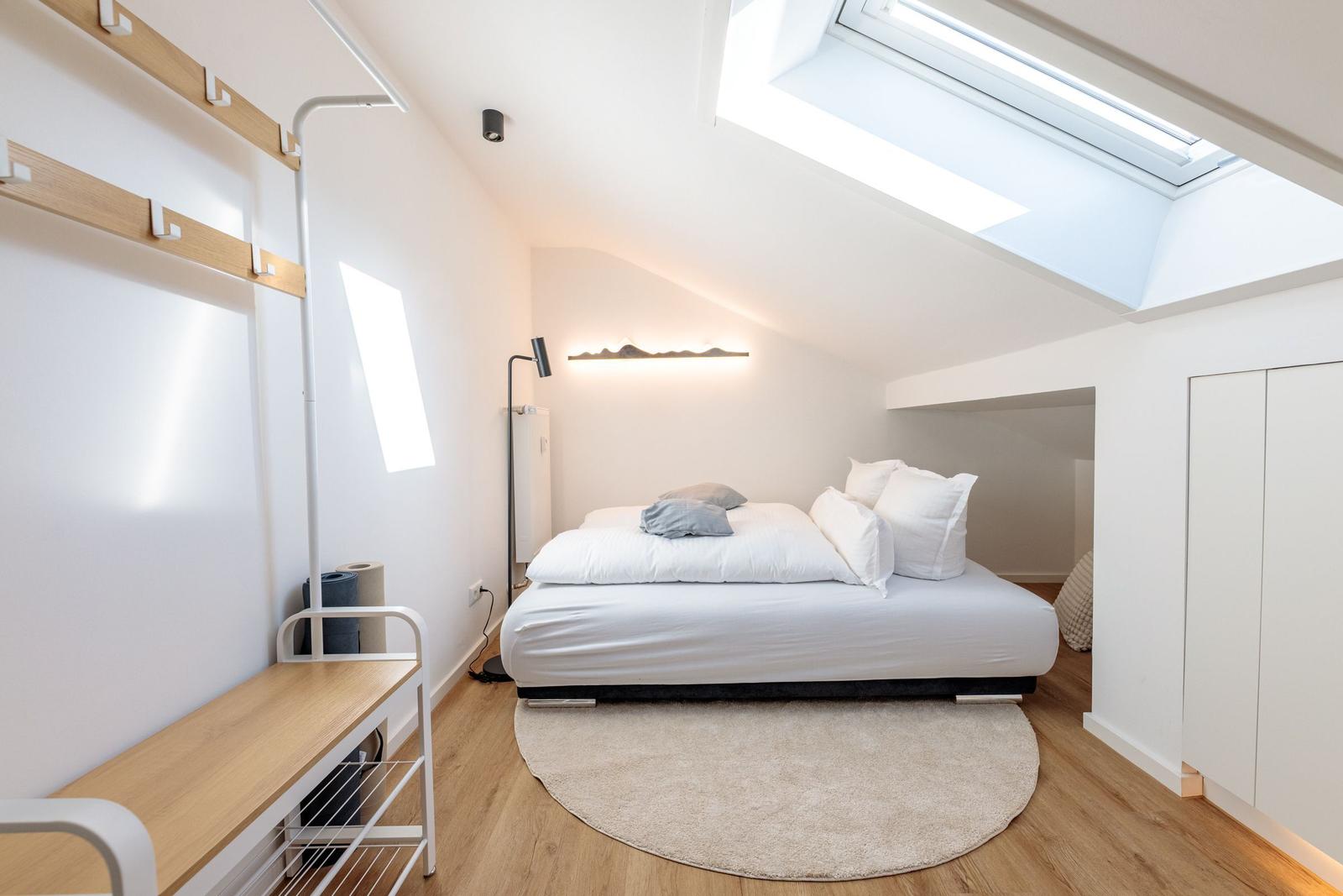 Schlafzimmer mit Dachschrägen, Dachfenster, Bett und Kleiderständer.