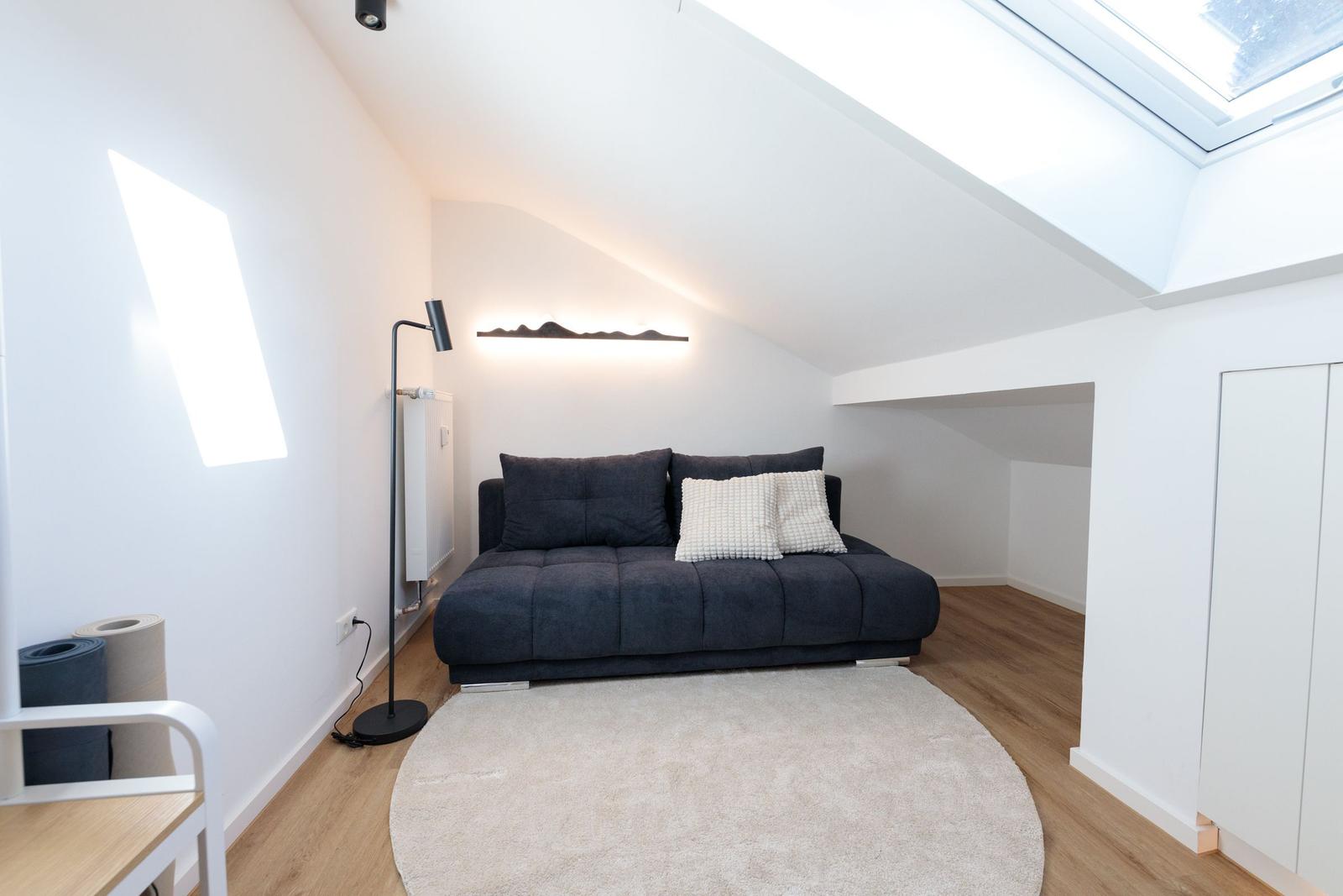 Schlafzimmer mit Dachschrägen, Sofa, Teppich und Dachfenster.