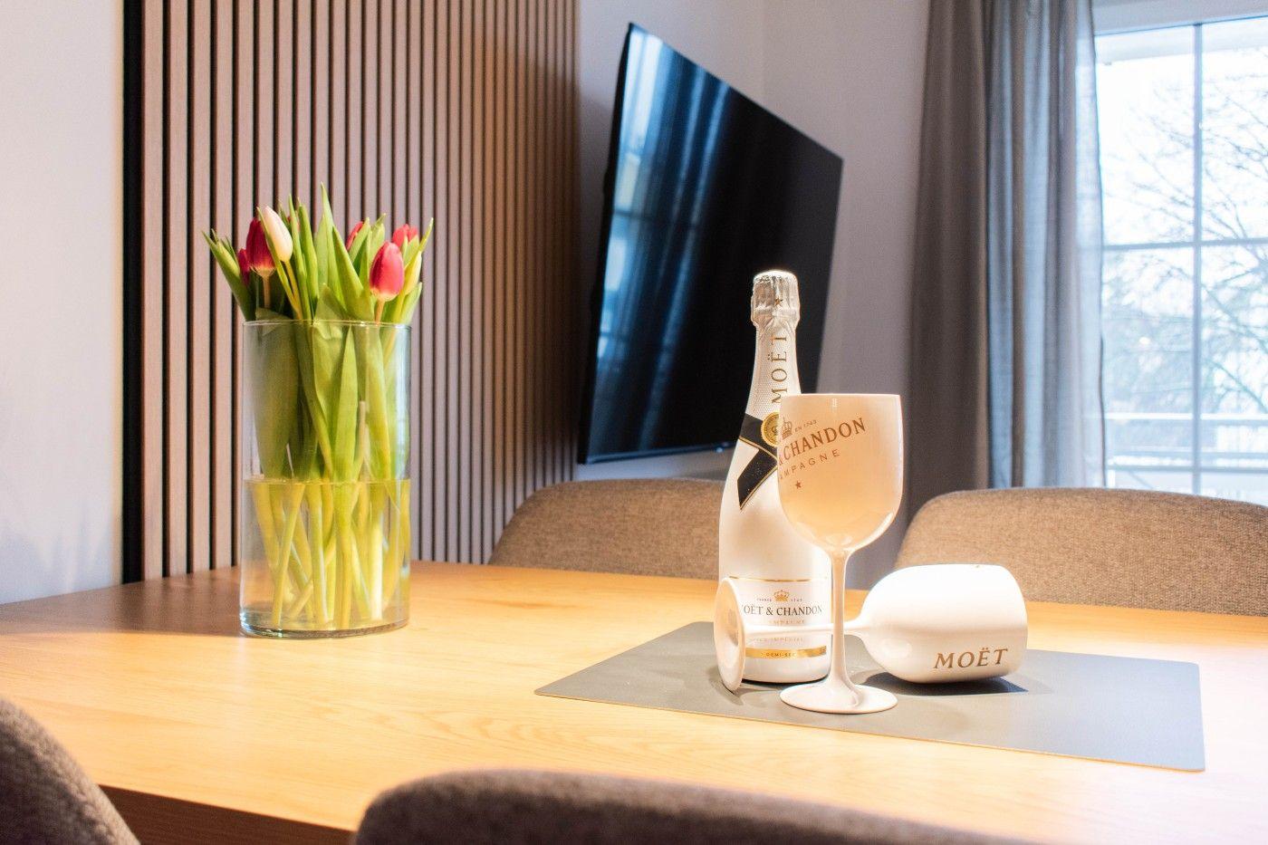 Tisch mit Tulpen, Sektflasche und Gläsern vor TV und Fenster