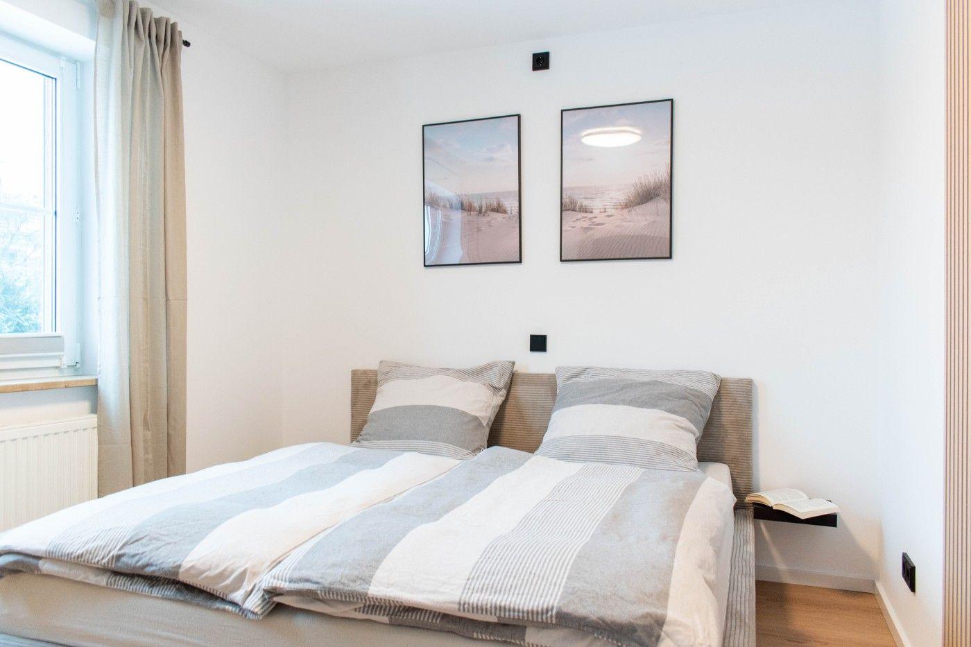 Schlafzimmer mit Bett, Fenster und Wandbildern.