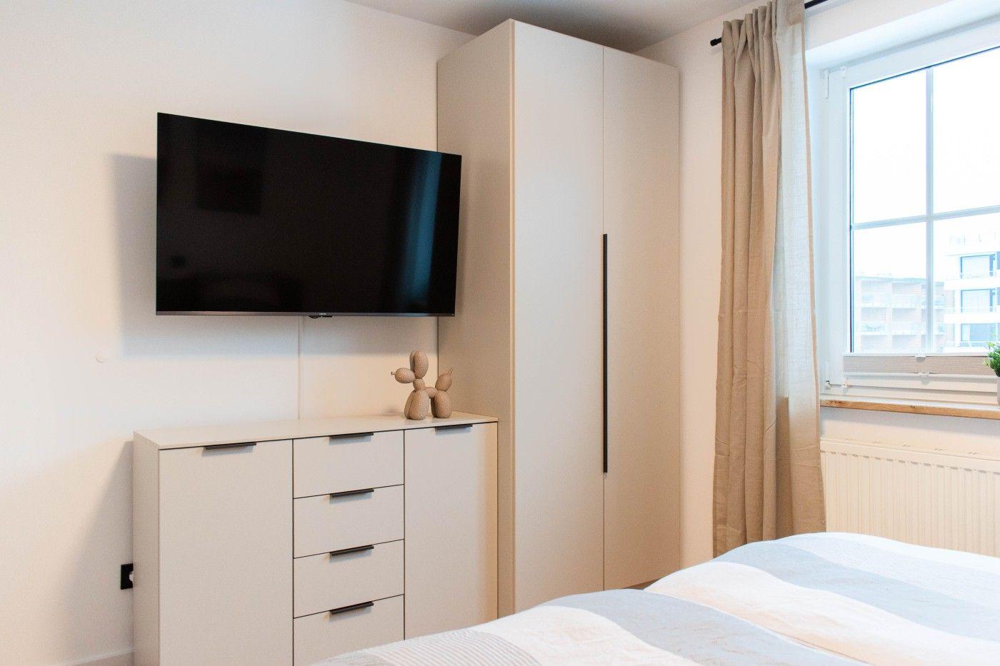 Schlafzimmer mit Bett, TV und Kleiderschrank. Fenster mit Vorhängen.