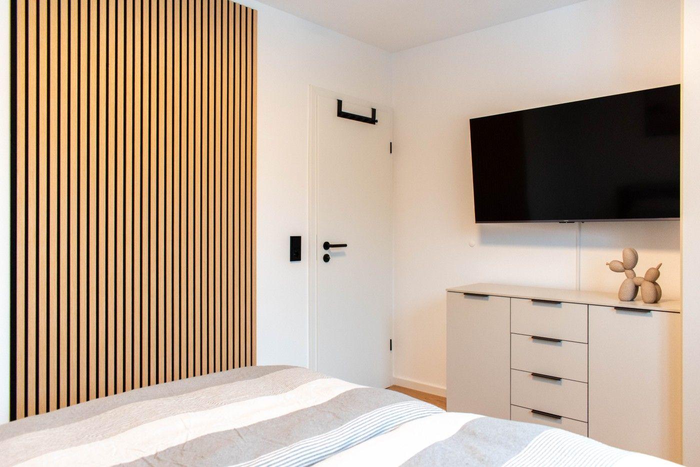 Schlafzimmer mit Bett, TV und Holzwand