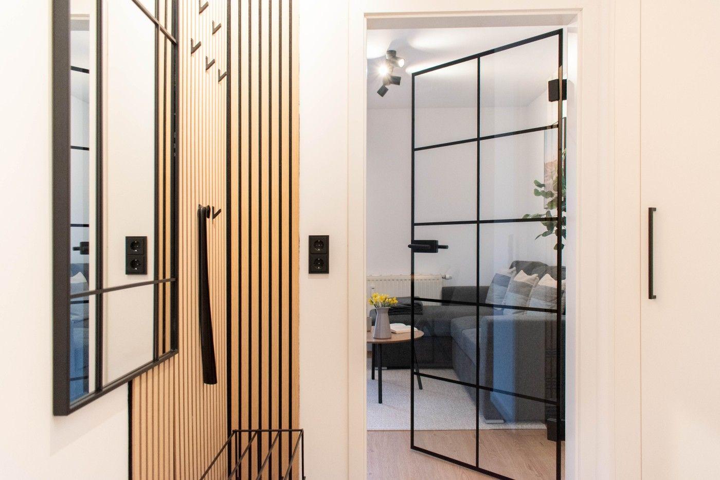 Eingangsbereich mit Holzvertäfelung und Glaswand zum Wohnzimmer mit Sofa und Tisch.